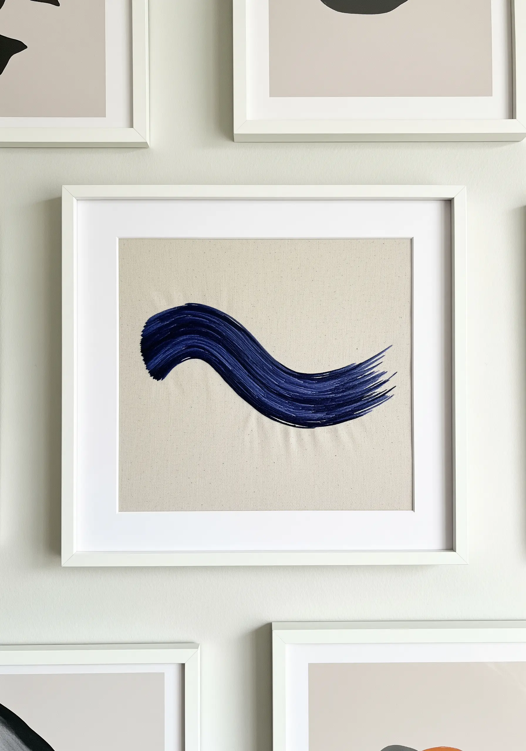 A framed embroidery piece that mimics a single, wide blue paint brushstroke.