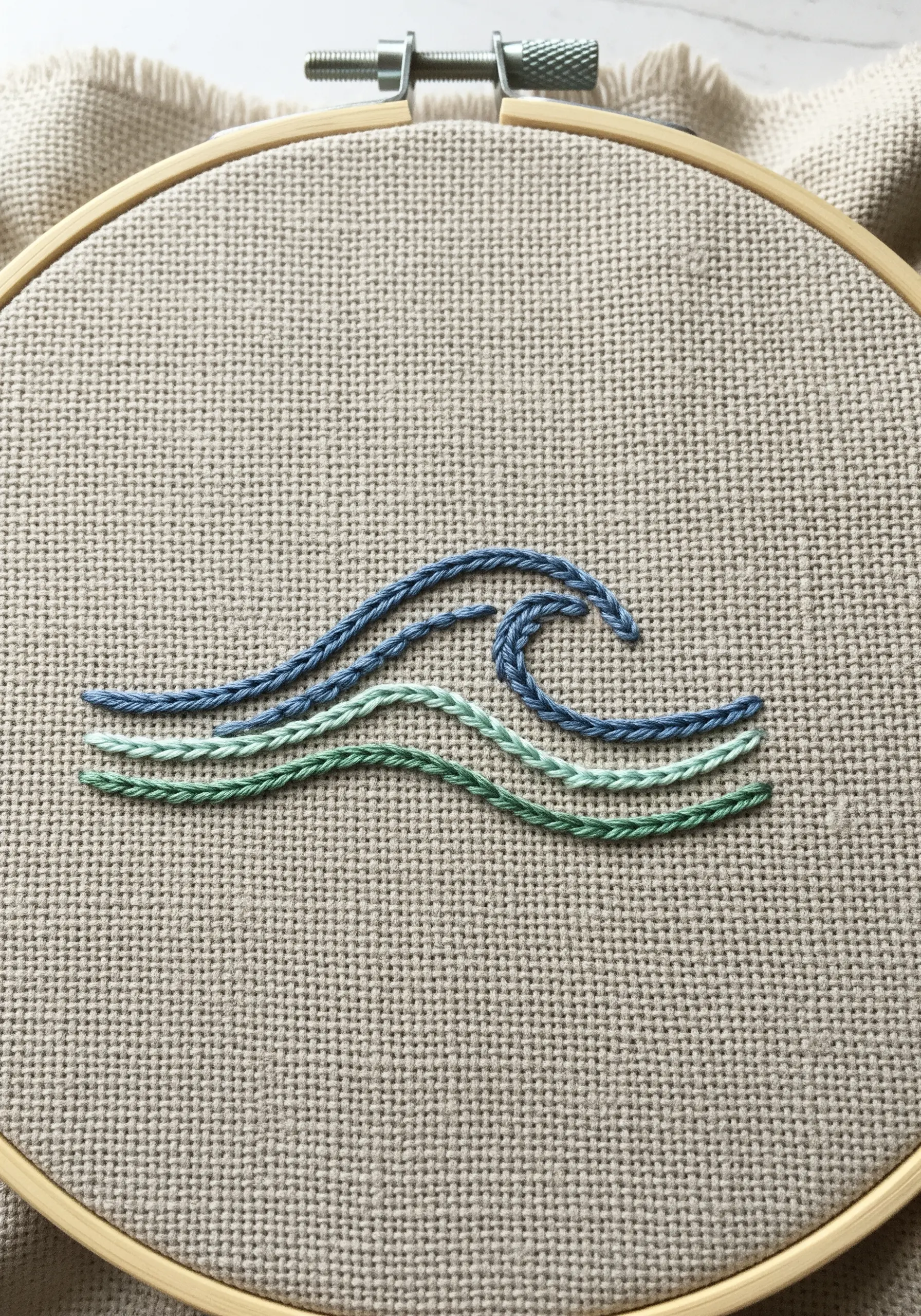 Four stylized waves stitched in shades of blue and green using a textured stitch.