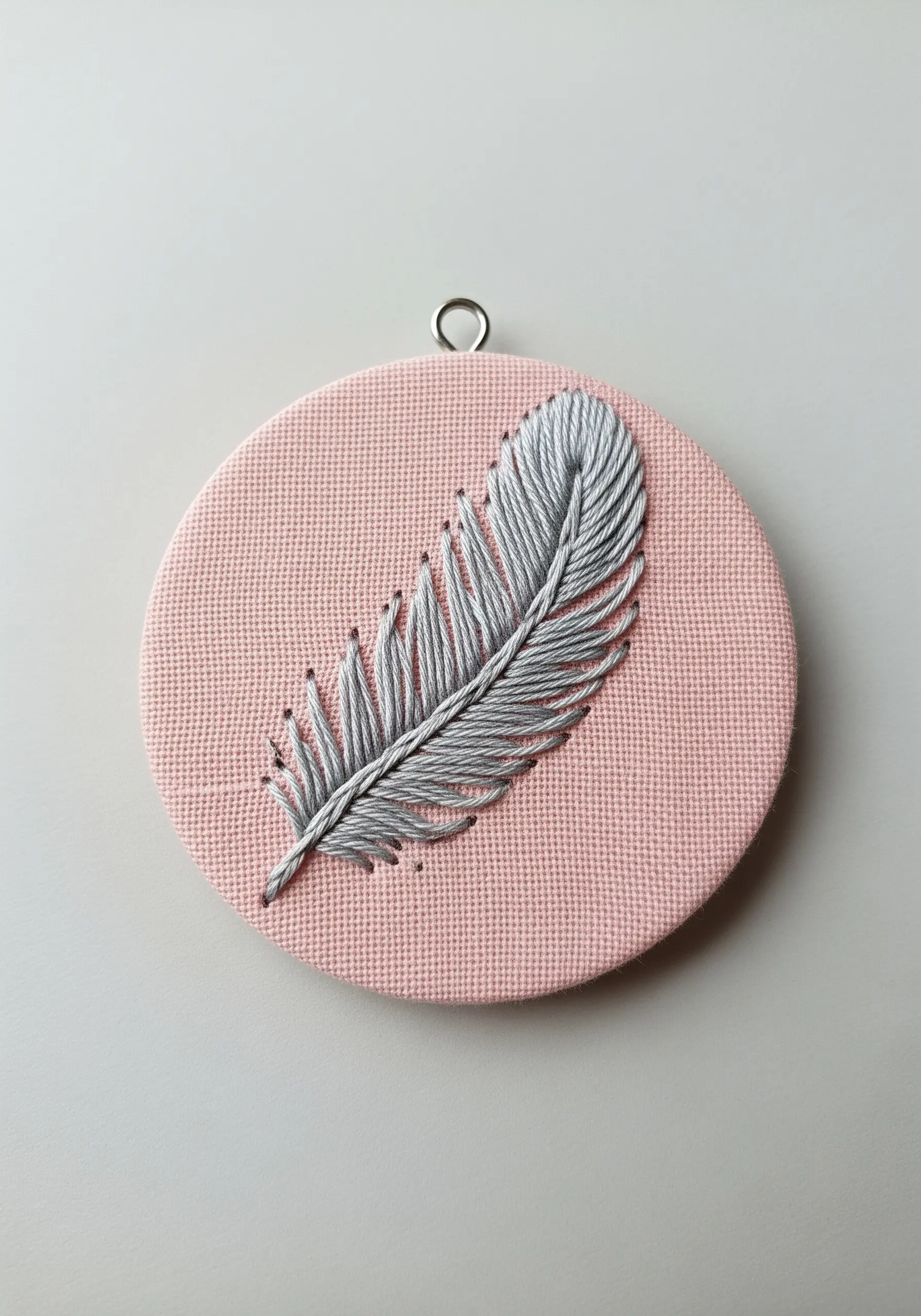 A grey embroidered feather using open fishbone stitch on a soft pink background.