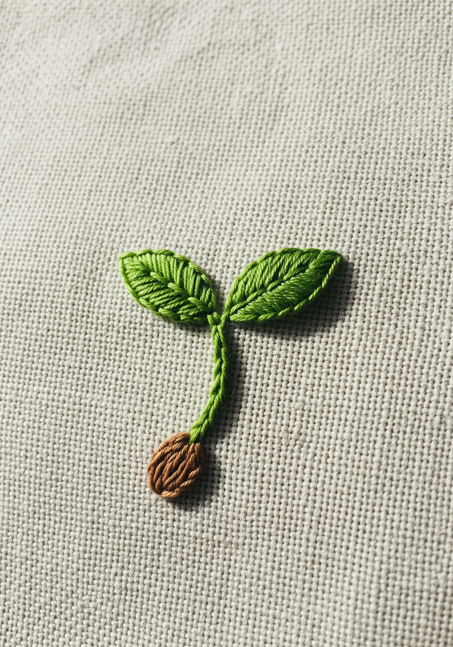 A close-up of a small embroidered sprout with two green leaves and a brown seed.