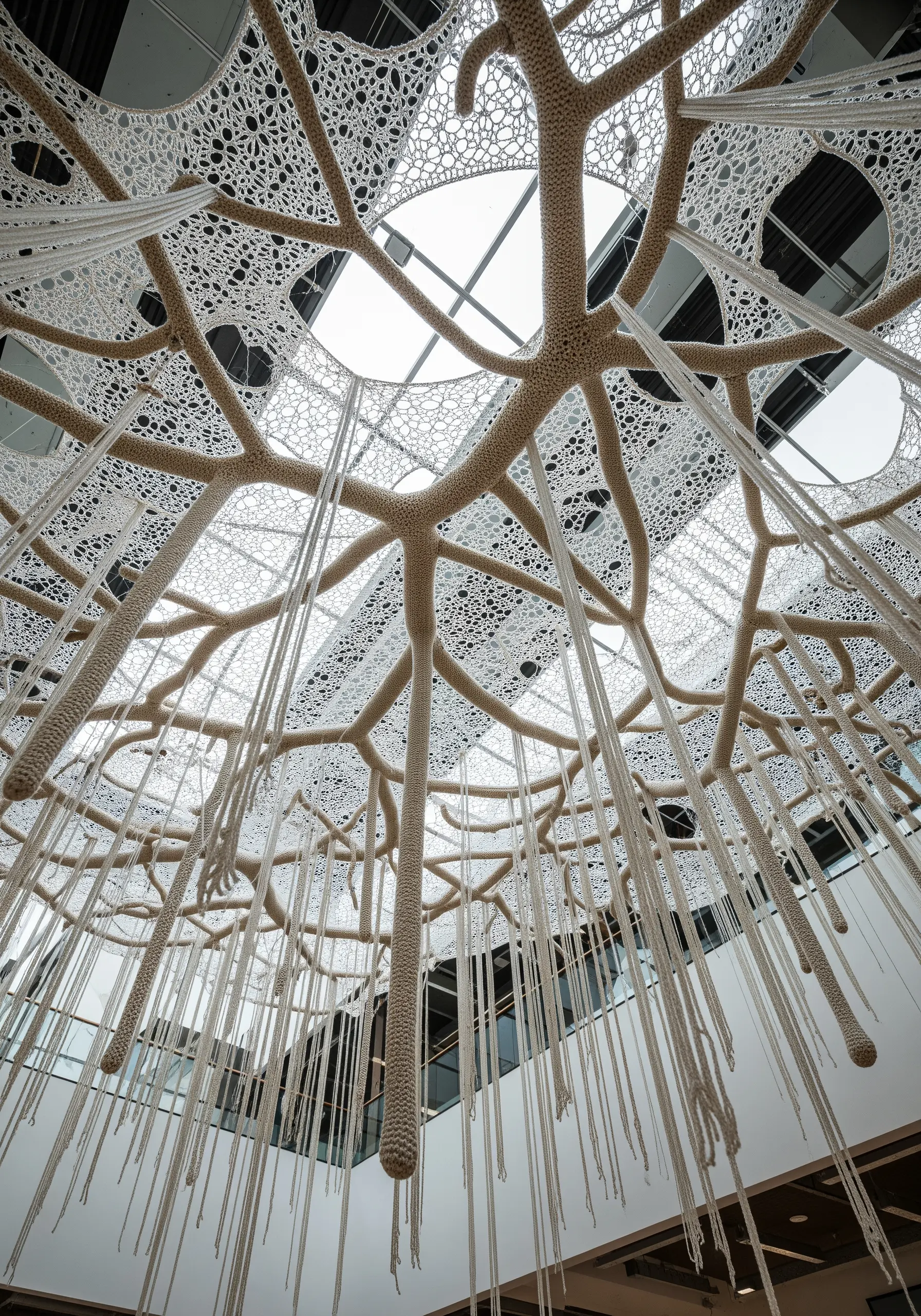 A large, white crocheted structure resembling tree roots or branches, spreading across a ceiling.