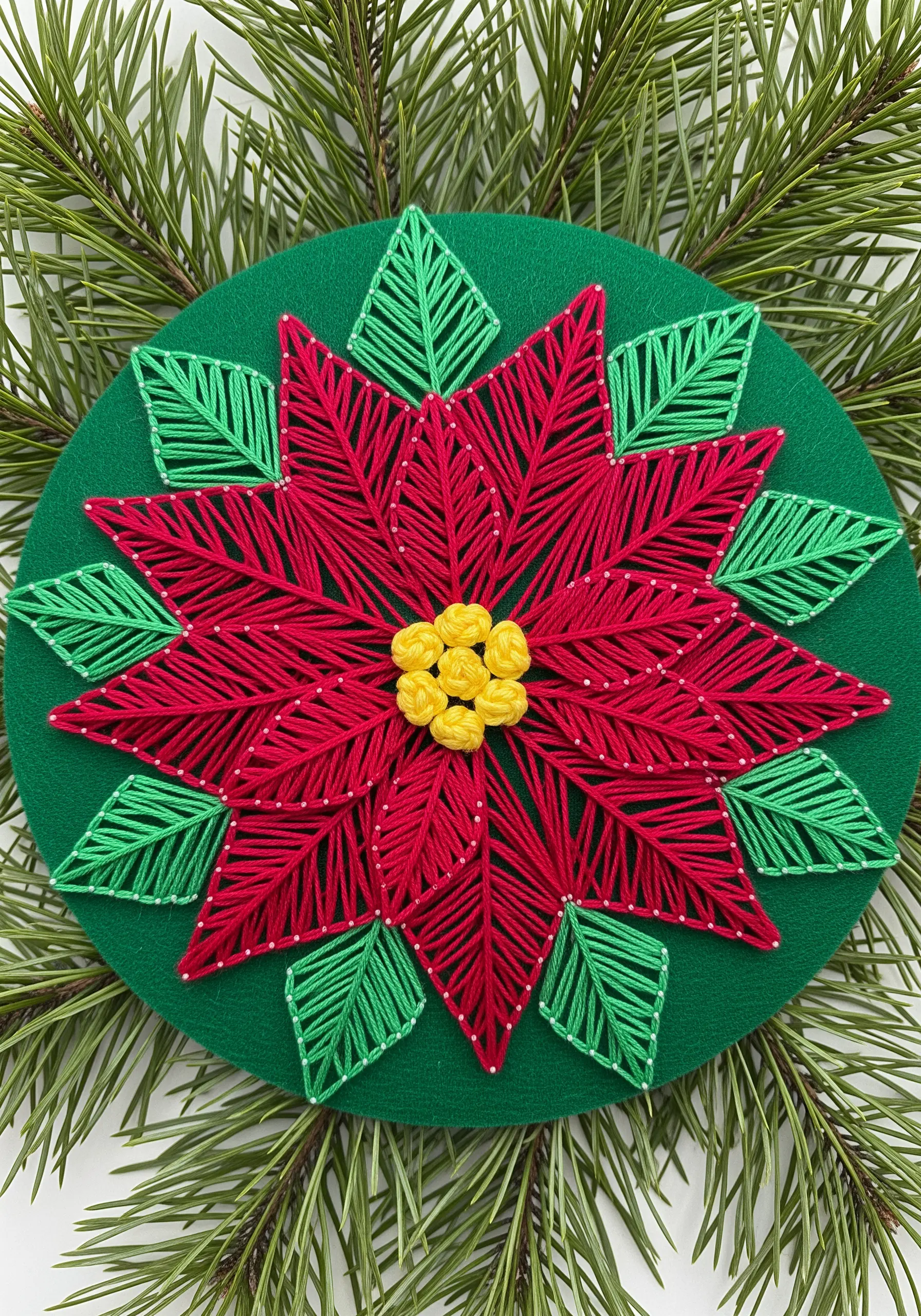 Red and green string art poinsettia with yellow French knot details.