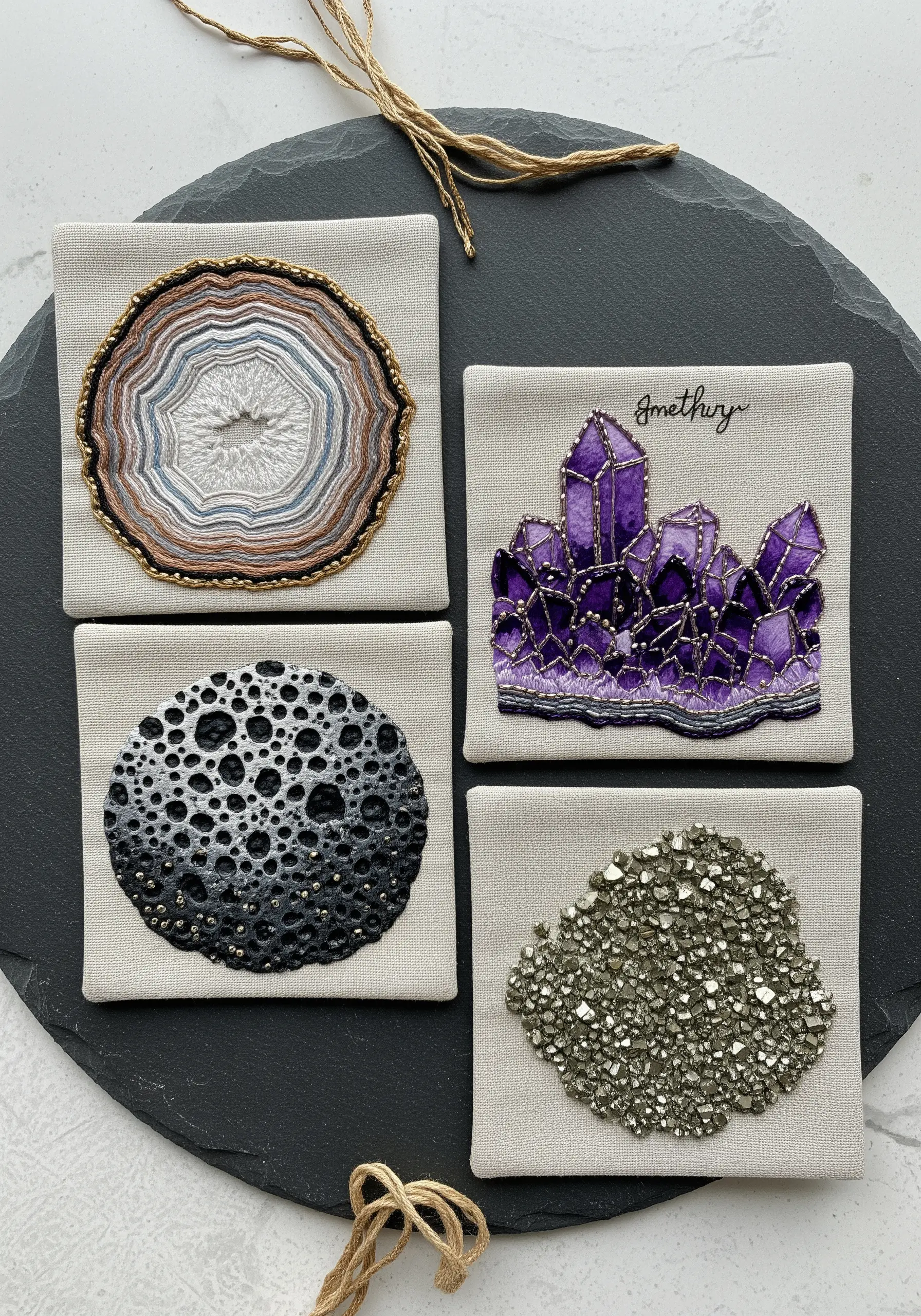 Four small embroidered squares depicting amethyst, agate, pyrite, and a cratered texture.