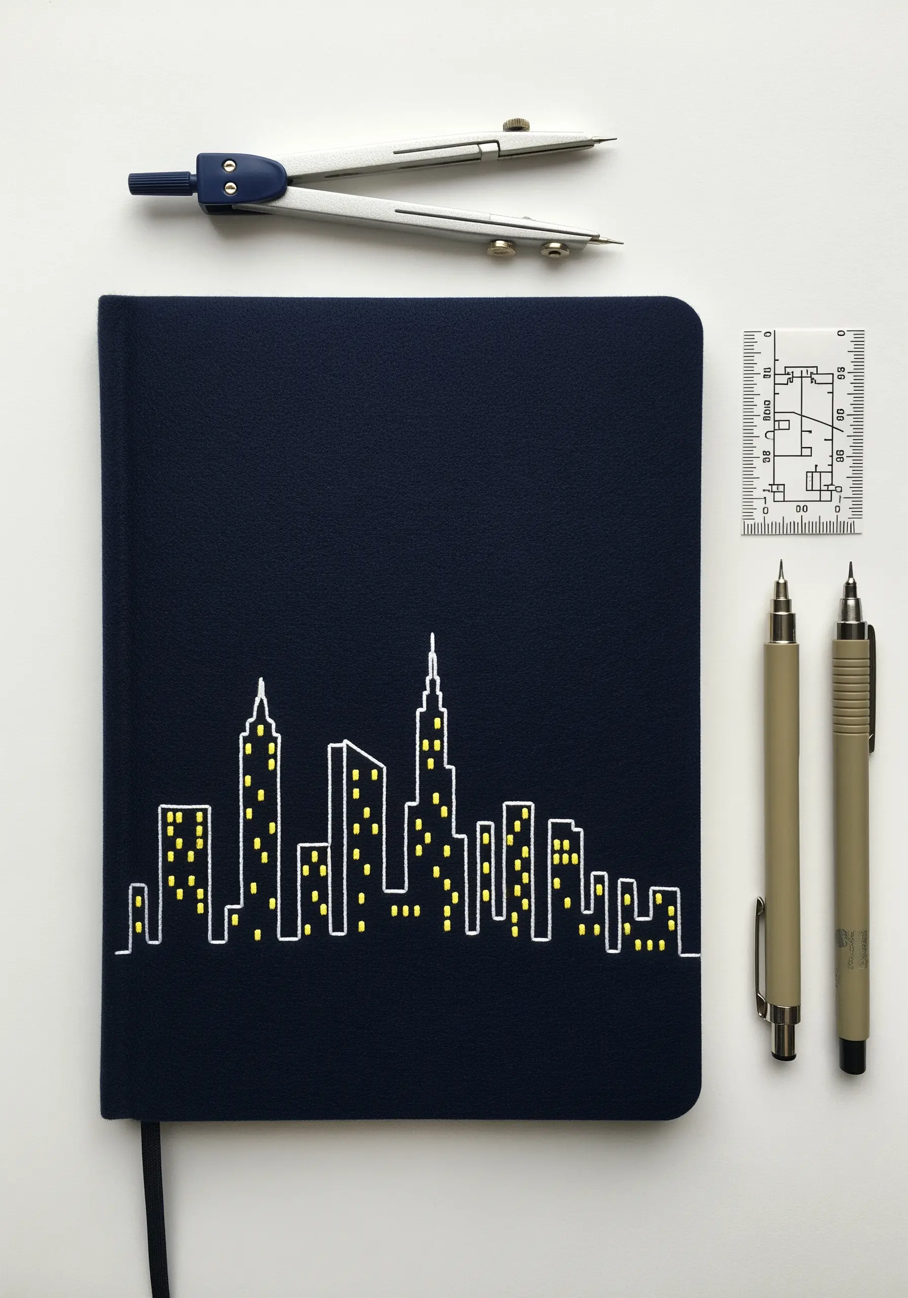 A minimalist embroidered cityscape in white outline with yellow stitched windows on a dark blue journal.