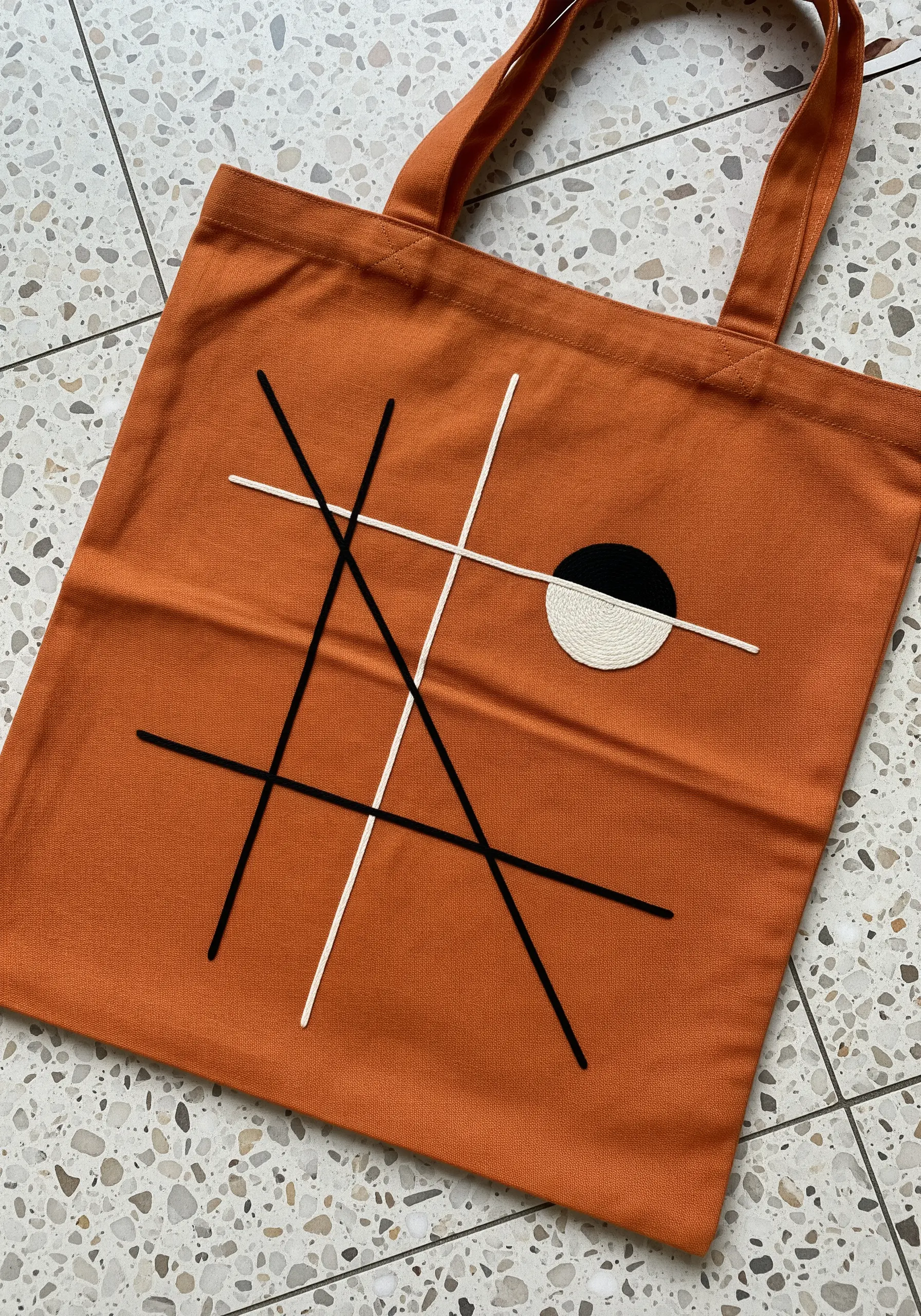Abstract black and white lines intersecting with a half-filled circle on a rust-colored tote.