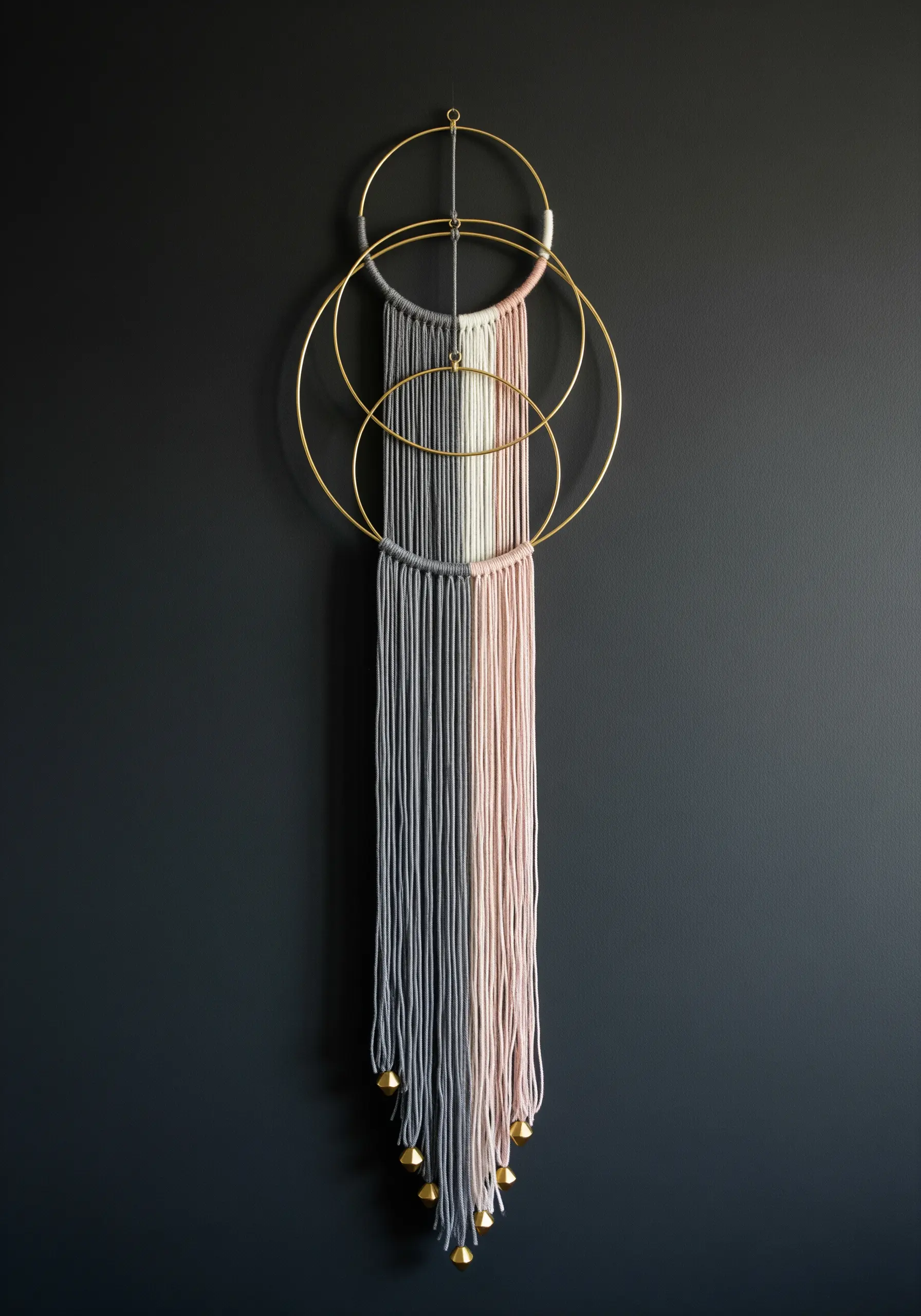 Modern wall hanging made of interlocking brass hoops wrapped in grey and pink yarn.