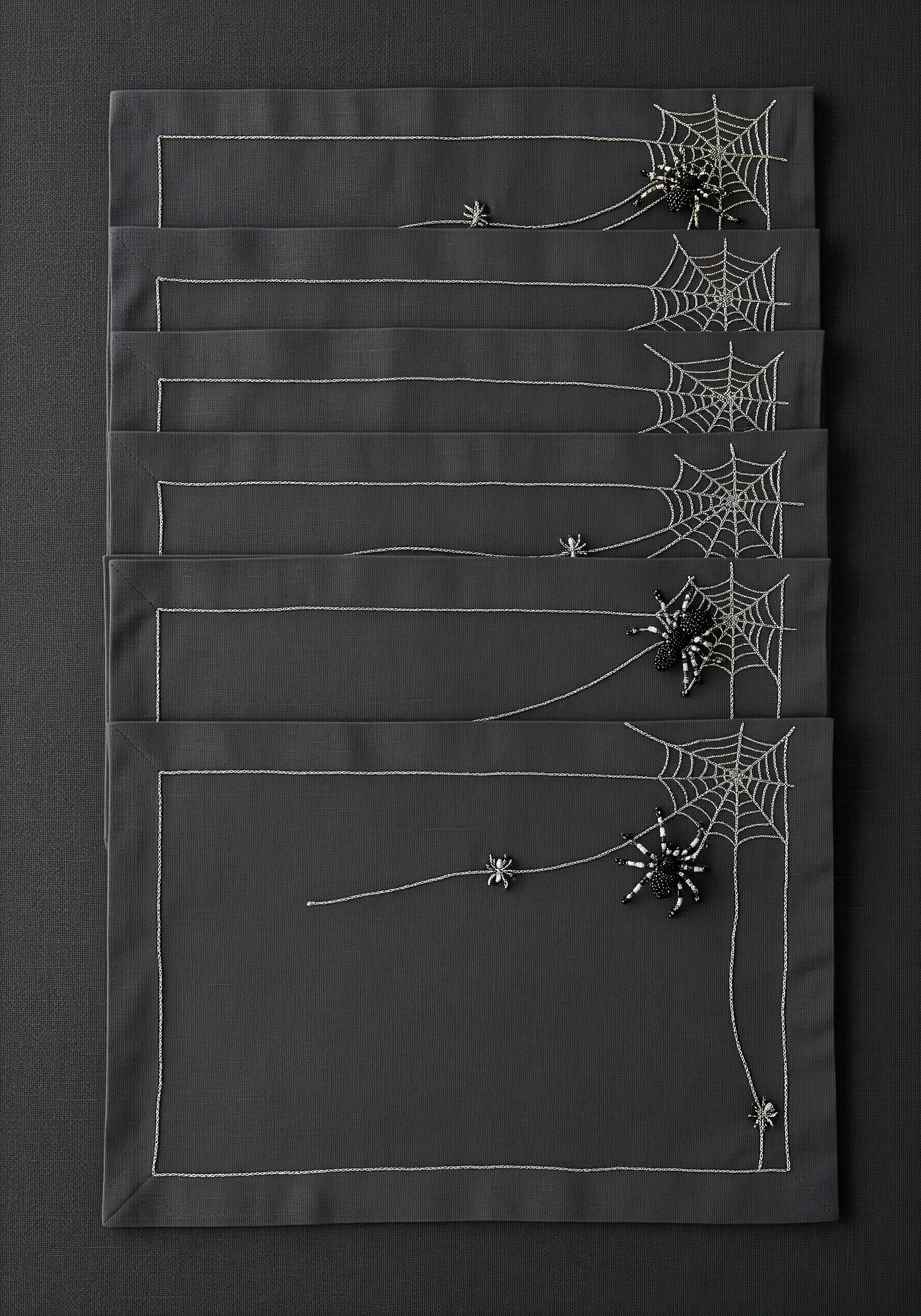 Minimalist spiderweb embroidery with 3D beaded spiders on gray placemats.