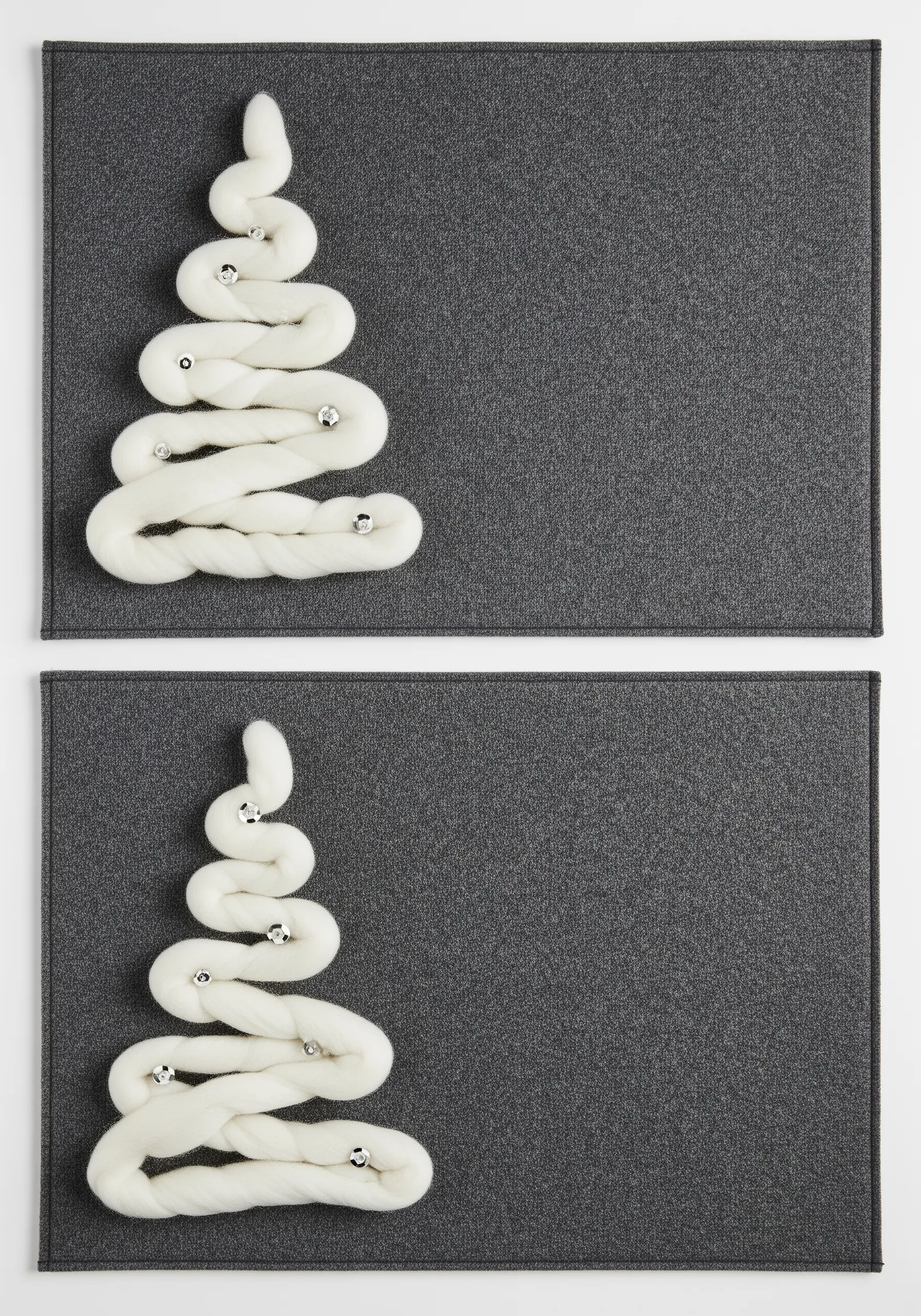 A minimalist Christmas tree made from couched white wool roving on a dark gray placemat.