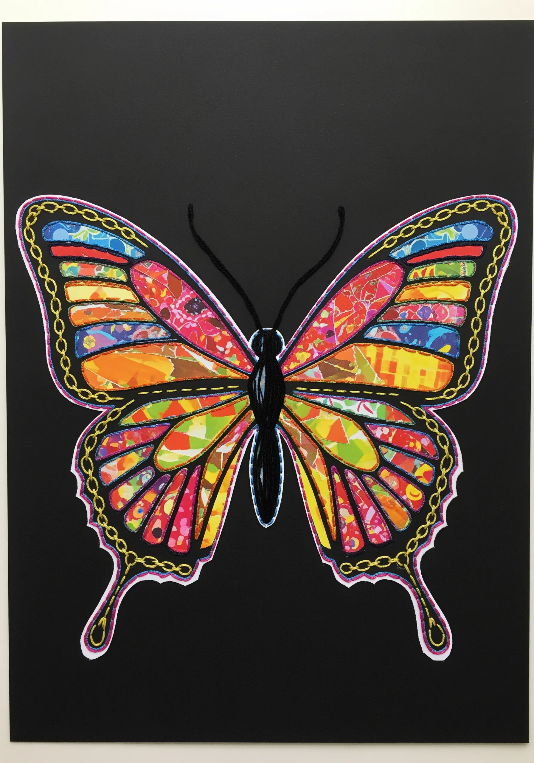 A colorful butterfly made from paper collage, outlined with gold chain stitch embroidery.