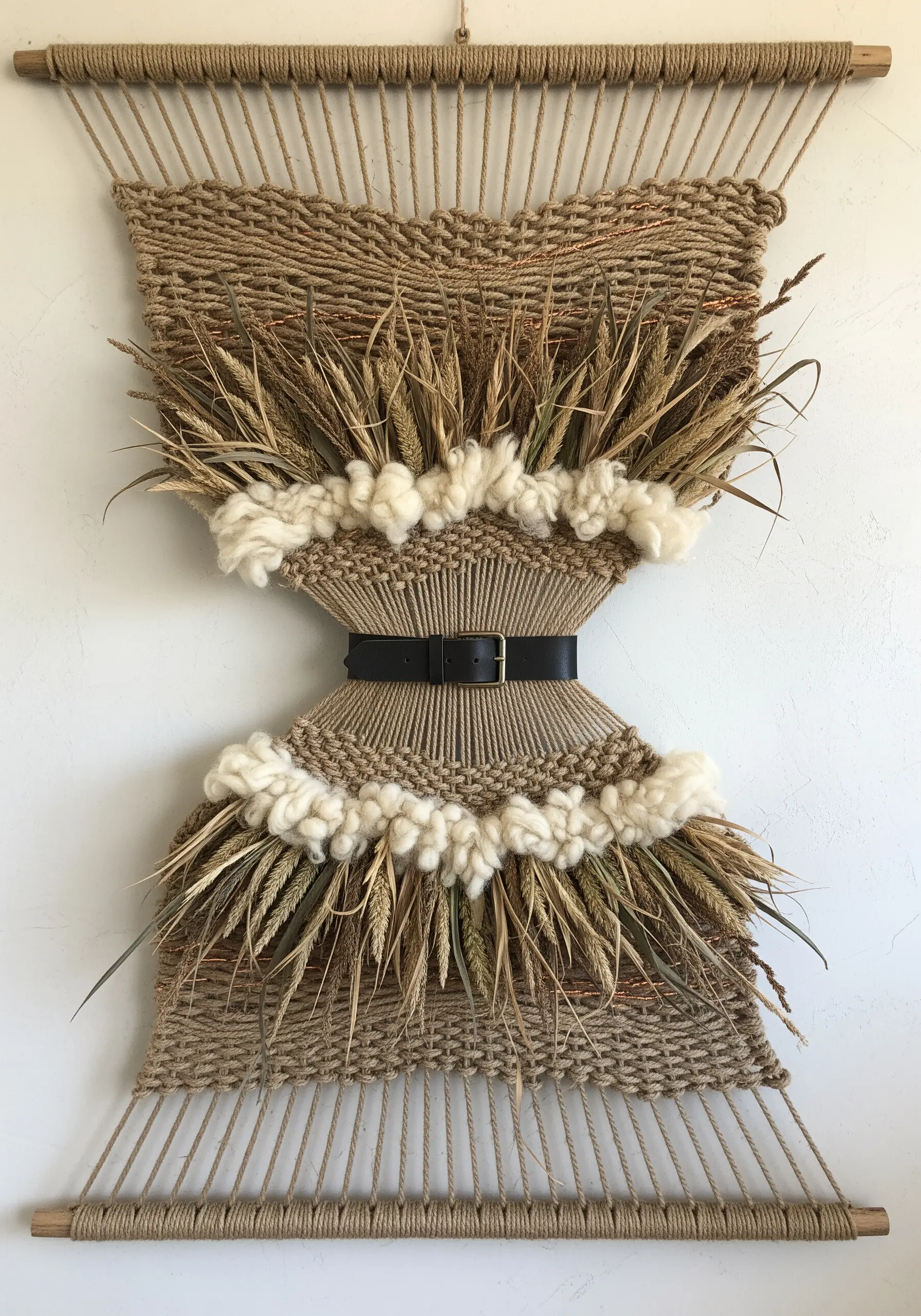Woven wall hanging featuring dried wheat stalks and a leather belt