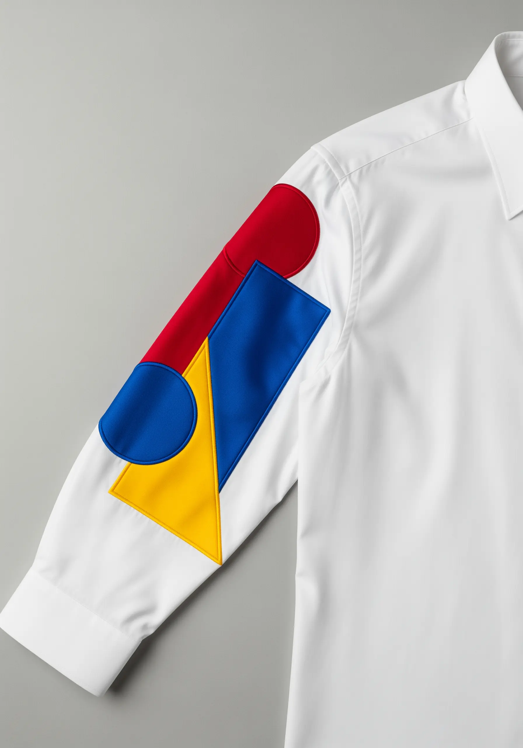 Bold, geometric appliqué shapes in red, yellow, and blue on the sleeve of a white shirt.
