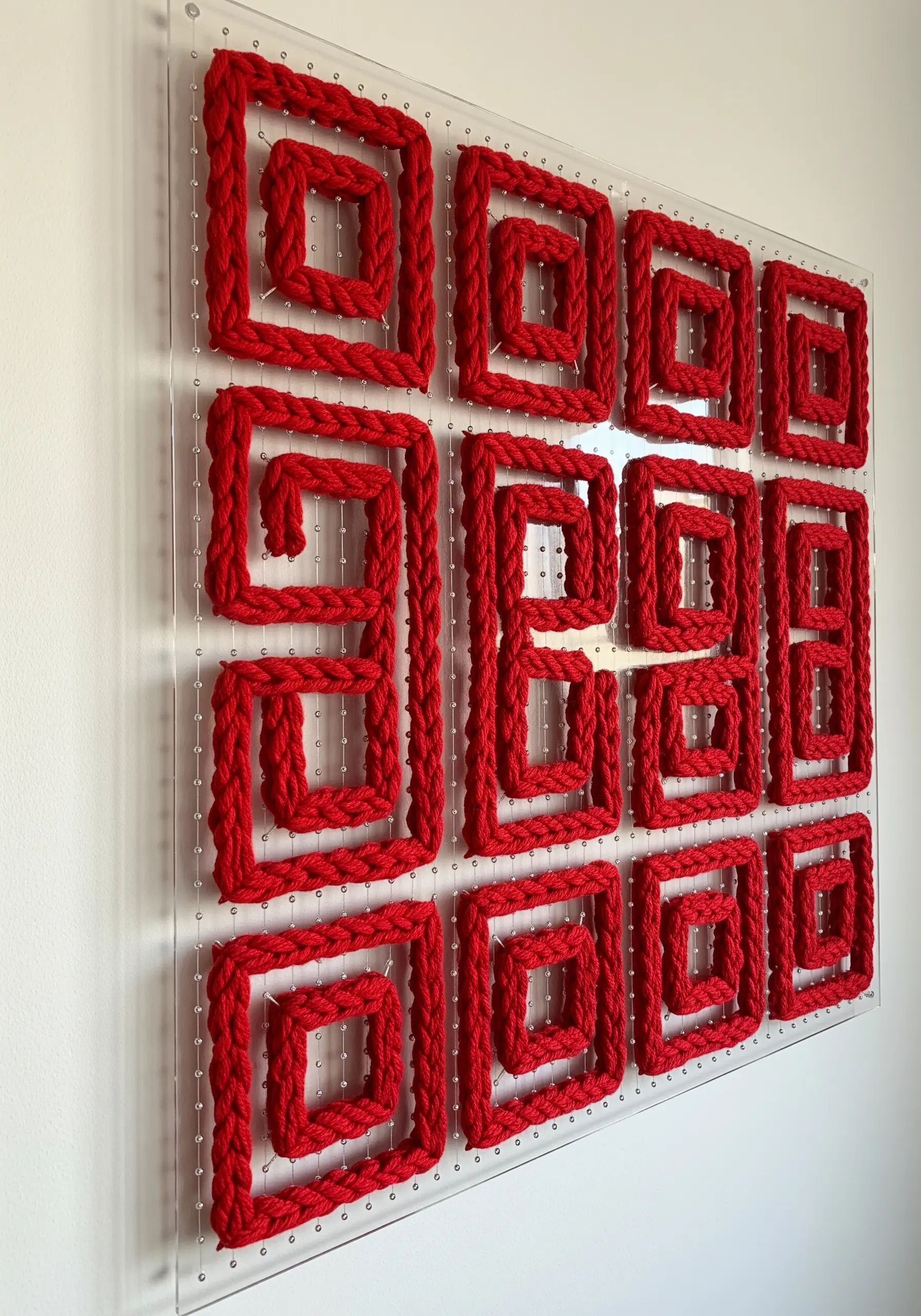 Geometric string art made with red cord woven through a clear acrylic grid board.