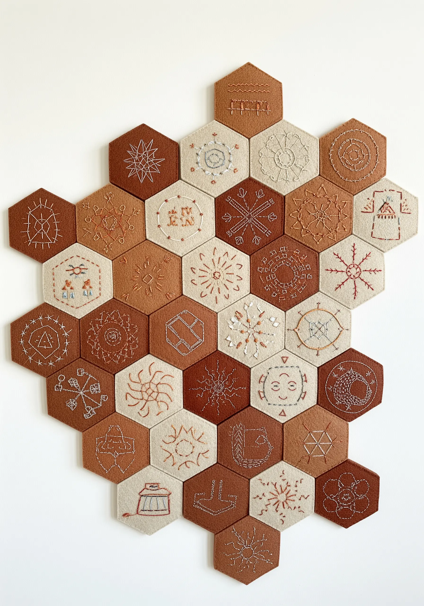 Hexagonal felt tiles with embroidered geometric patterns arranged on a wall