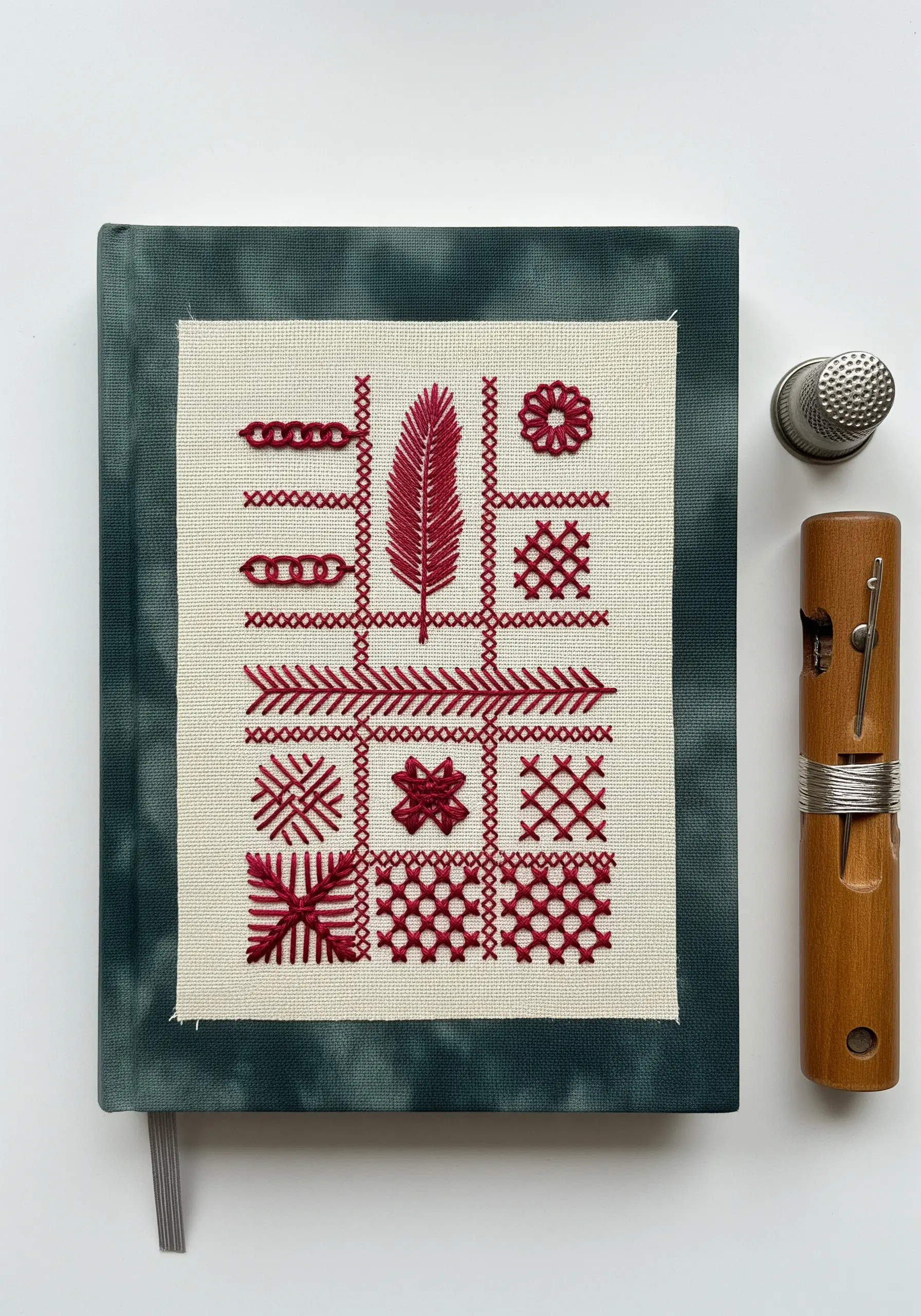 A redwork embroidery sampler featuring various stitch techniques, mounted on a dark green journal.