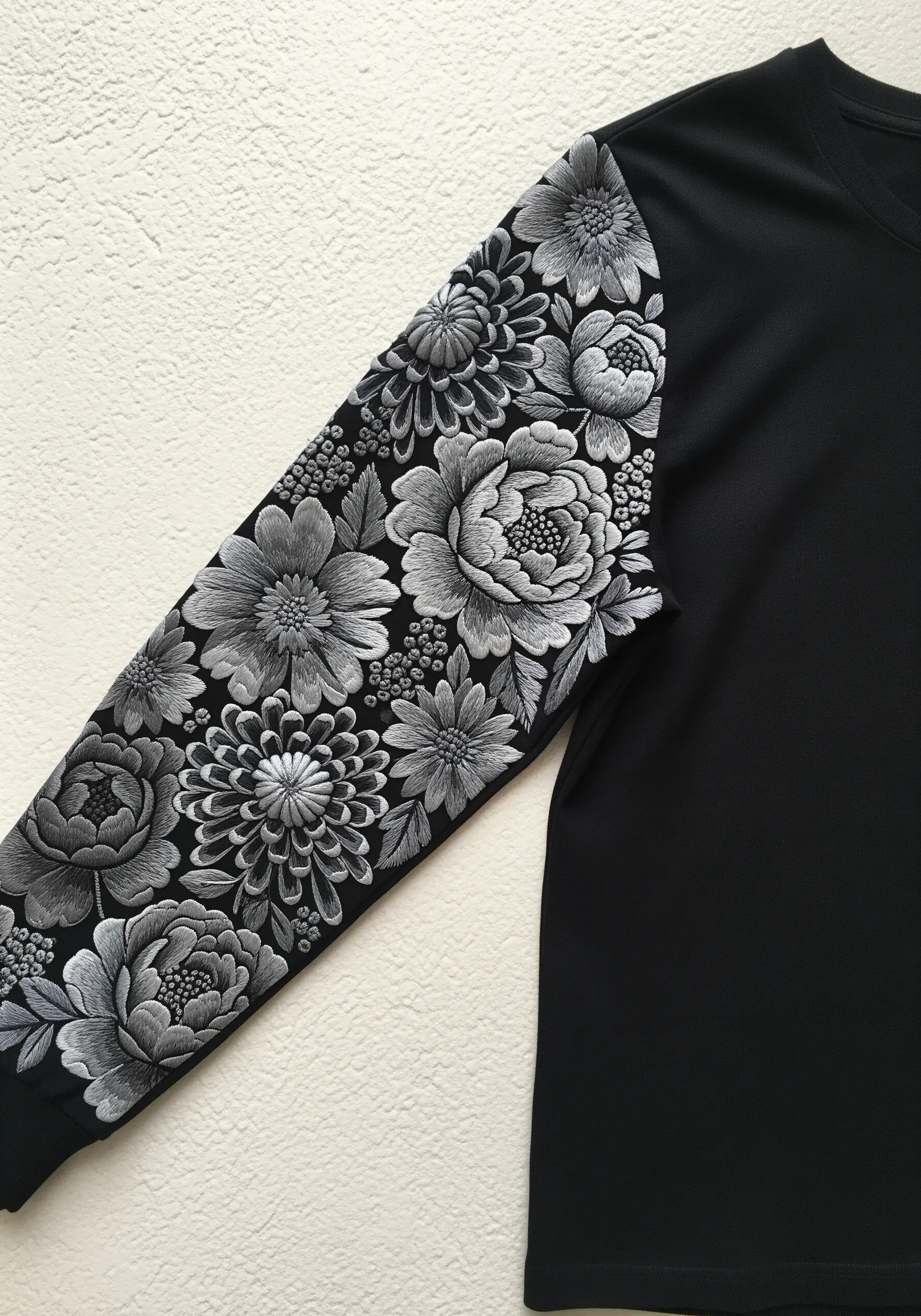 Highly detailed monochrome floral embroidery sleeve in shades of grey on a black shirt.