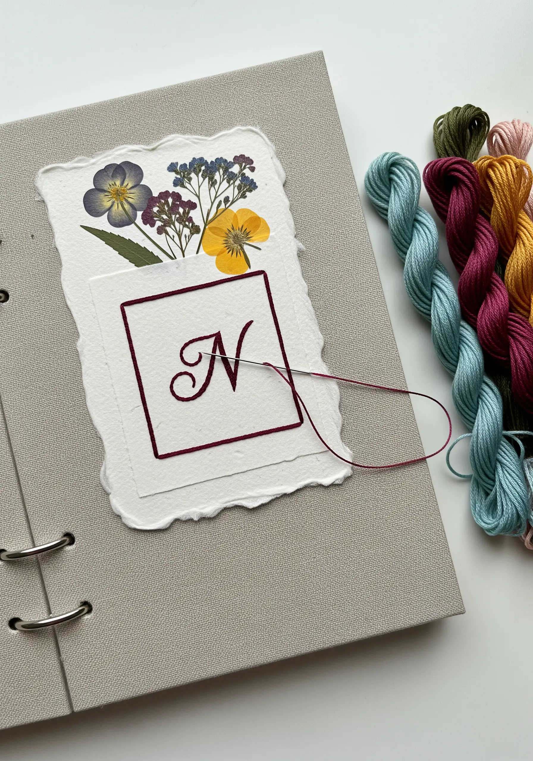 An embroidered monogram 'N' on paper, paired with dried pressed flowers.