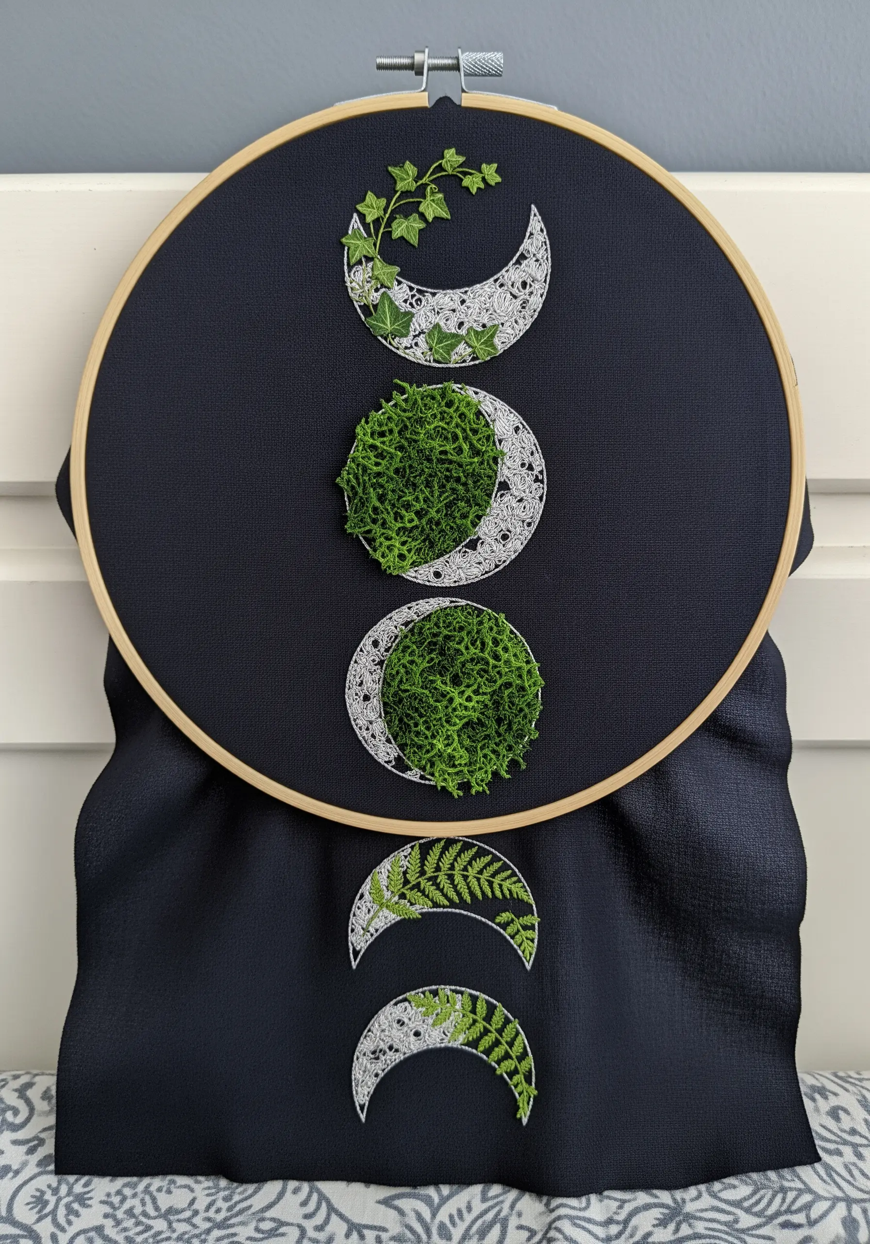 Moon phase embroidery combining white thread work with real moss and ferns.