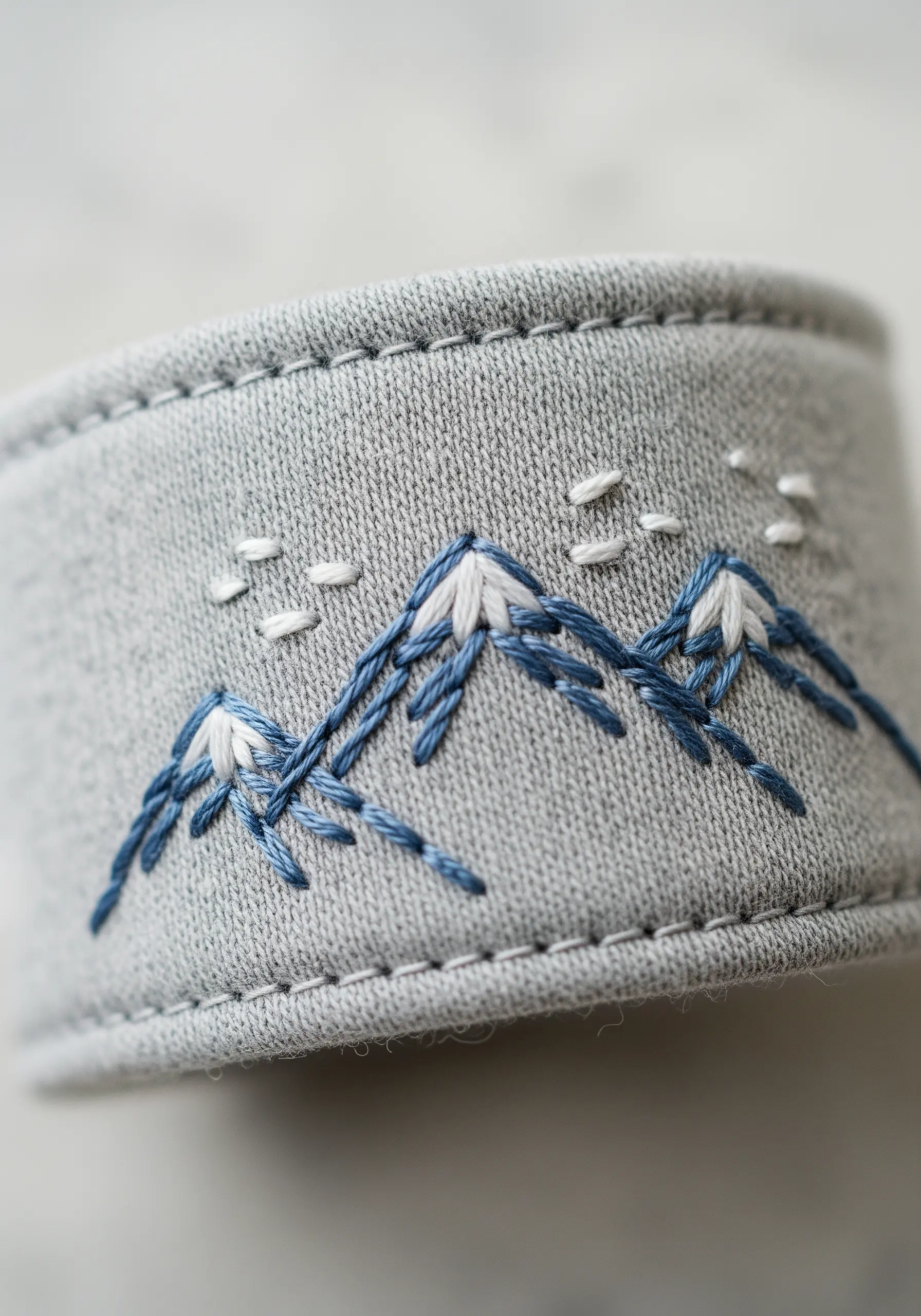 Embroidered mountain range on the grey ribbed cuff of a sleeve.