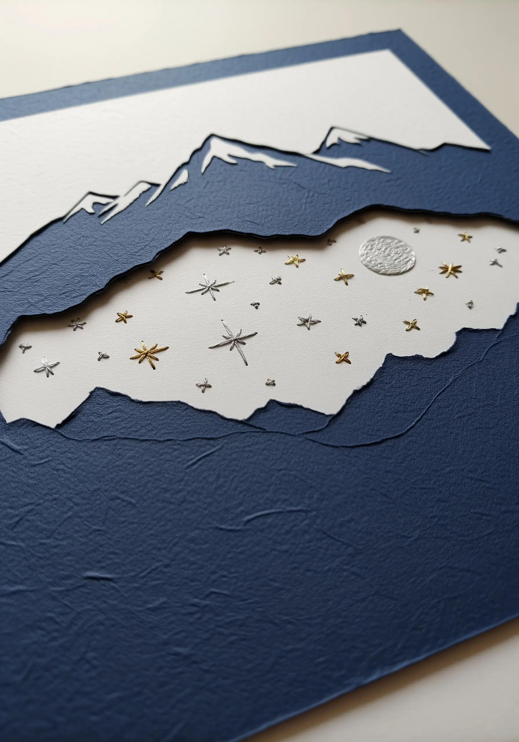 Cut paper mountain silhouette revealing a night sky with embroidered stars.