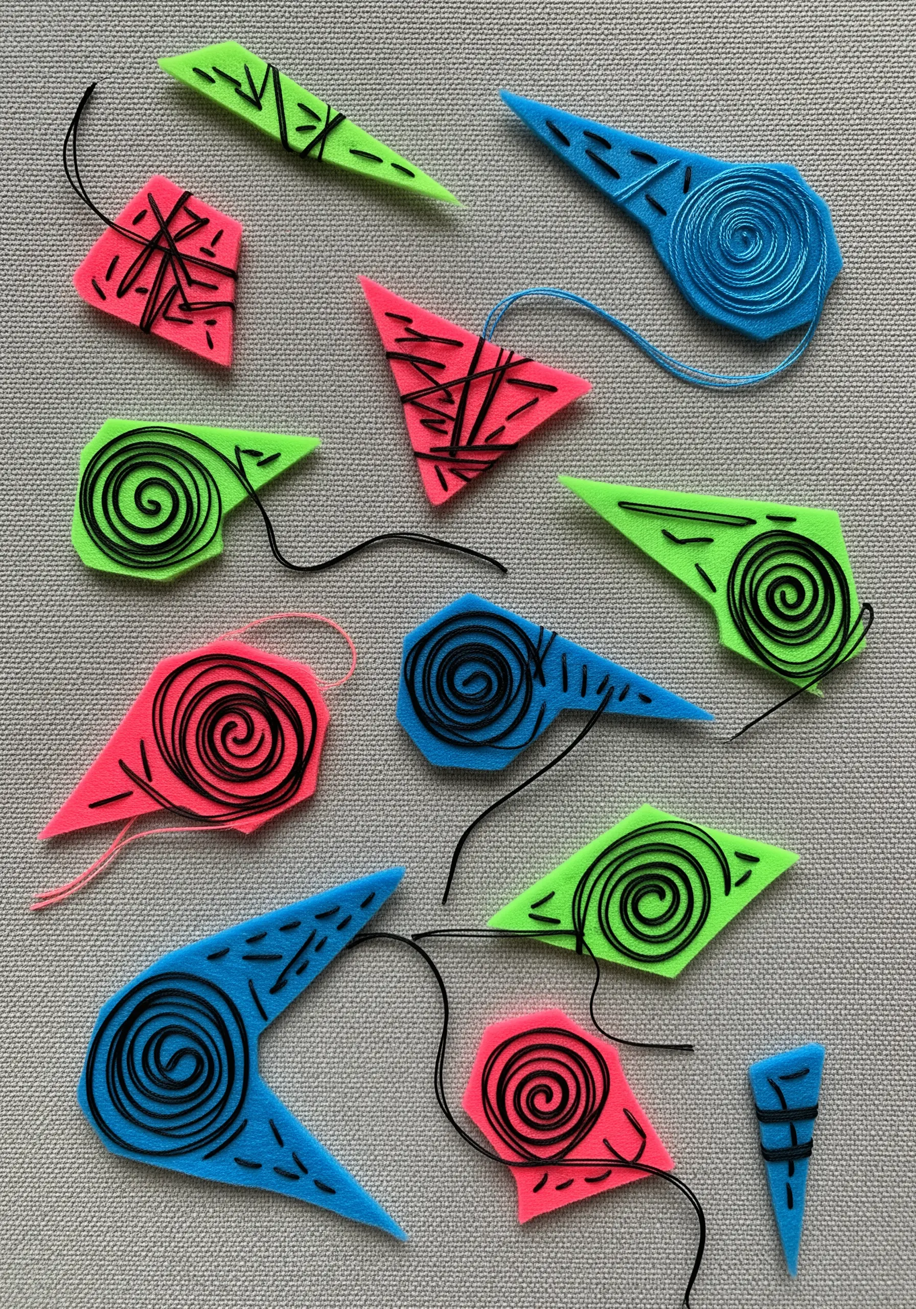 Bright neon felt shapes in pink, blue, and green with graphic black thread embroidery.