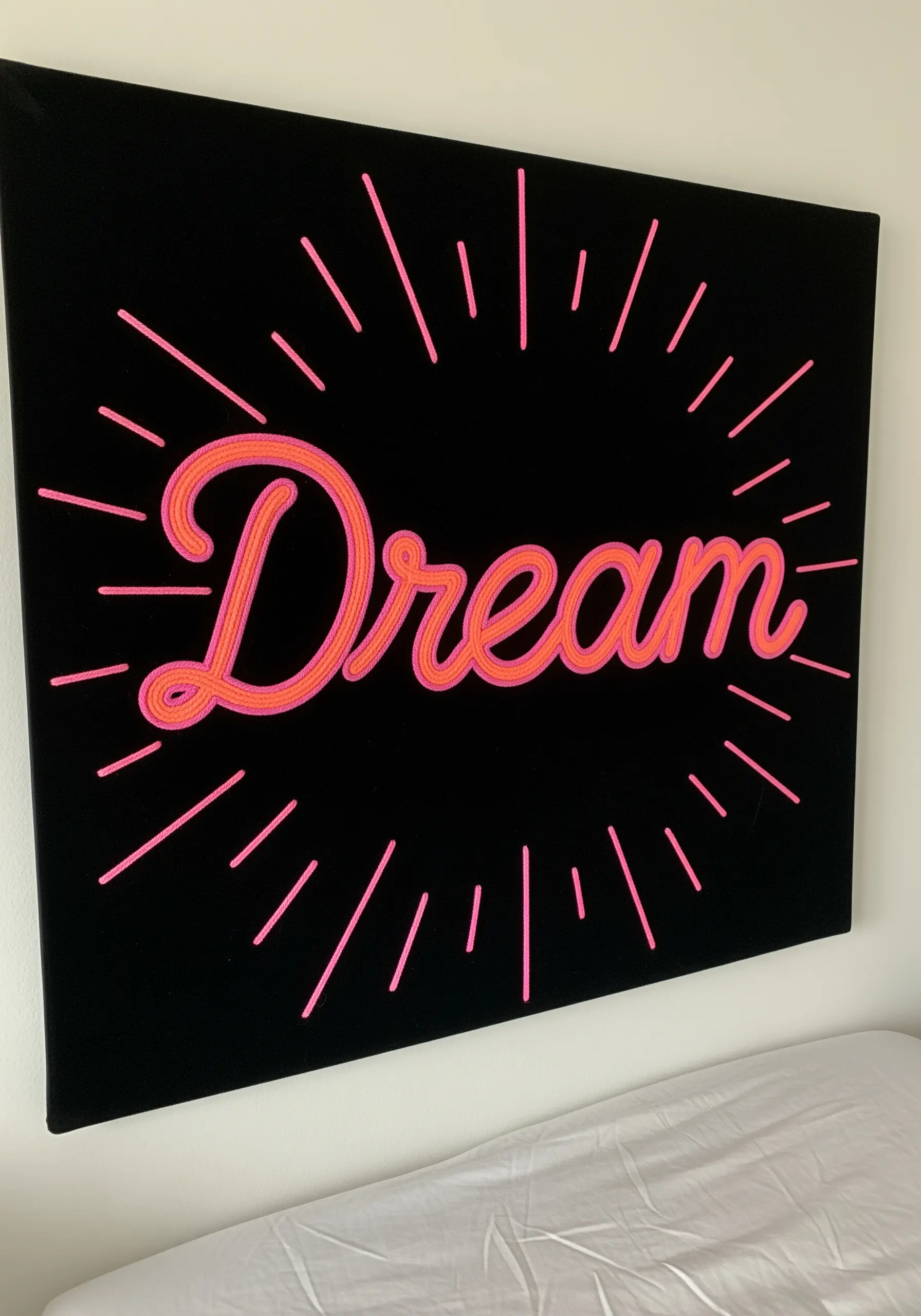 The word Dream embroidered in glowing pink script with radiating lines on black fabric.