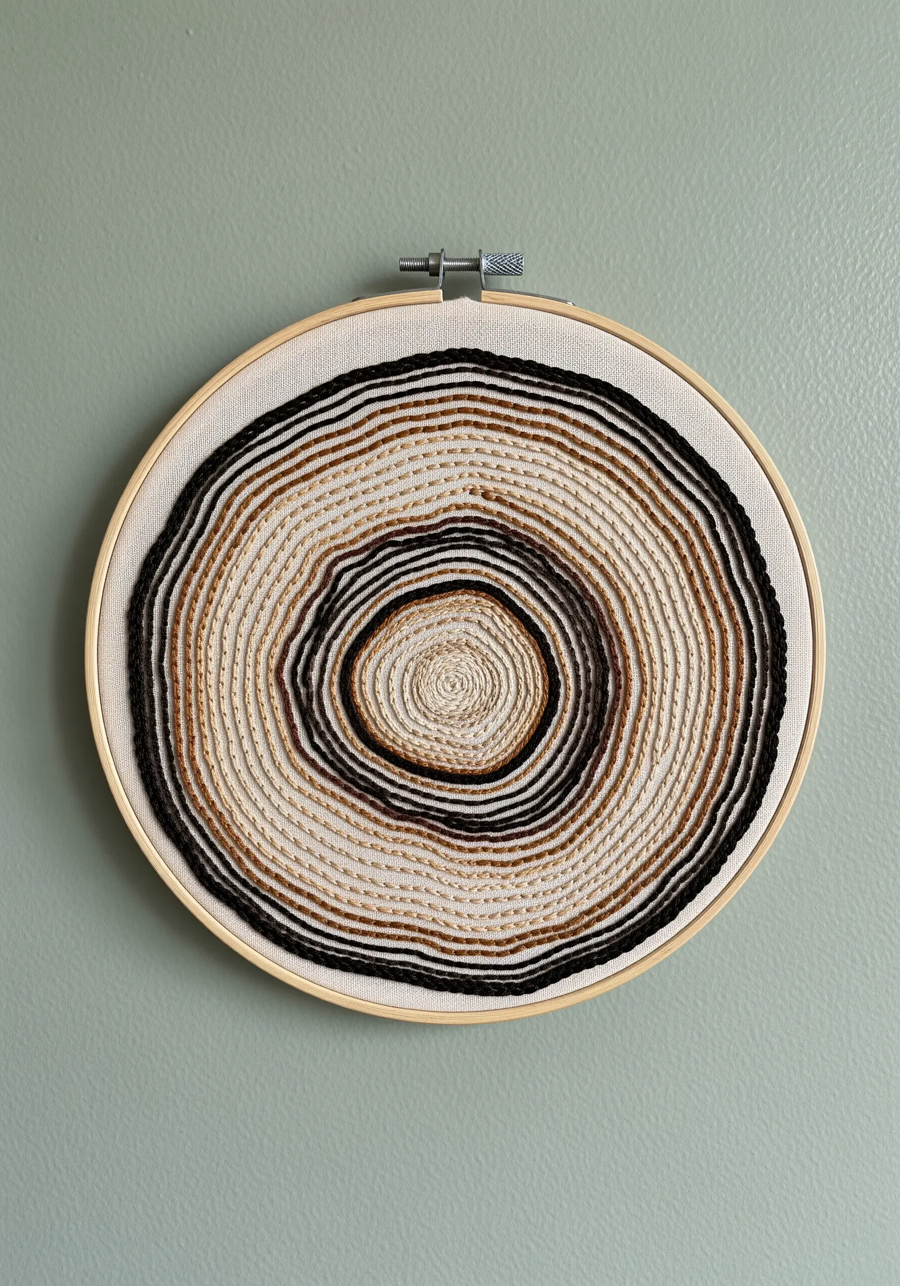 Embroidery hoop showing the concentric rings of a tree trunk in neutral-toned yarn and thread.
