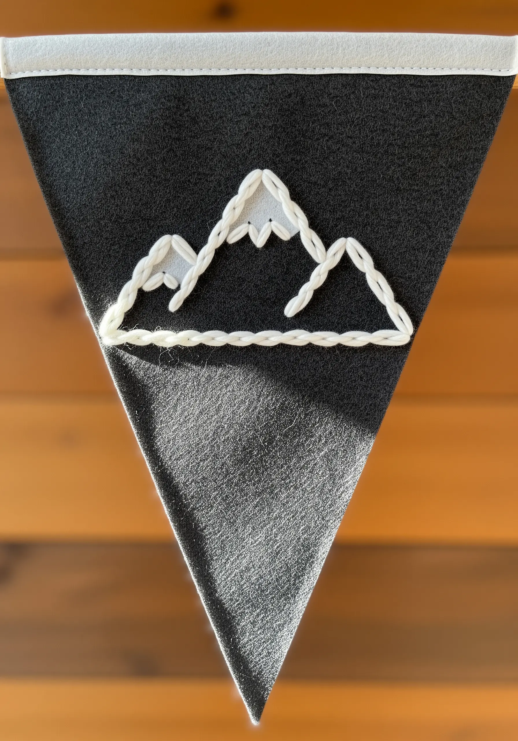 A mountain range outlined in chunky white chain stitch on a dark grey felt pennant.
