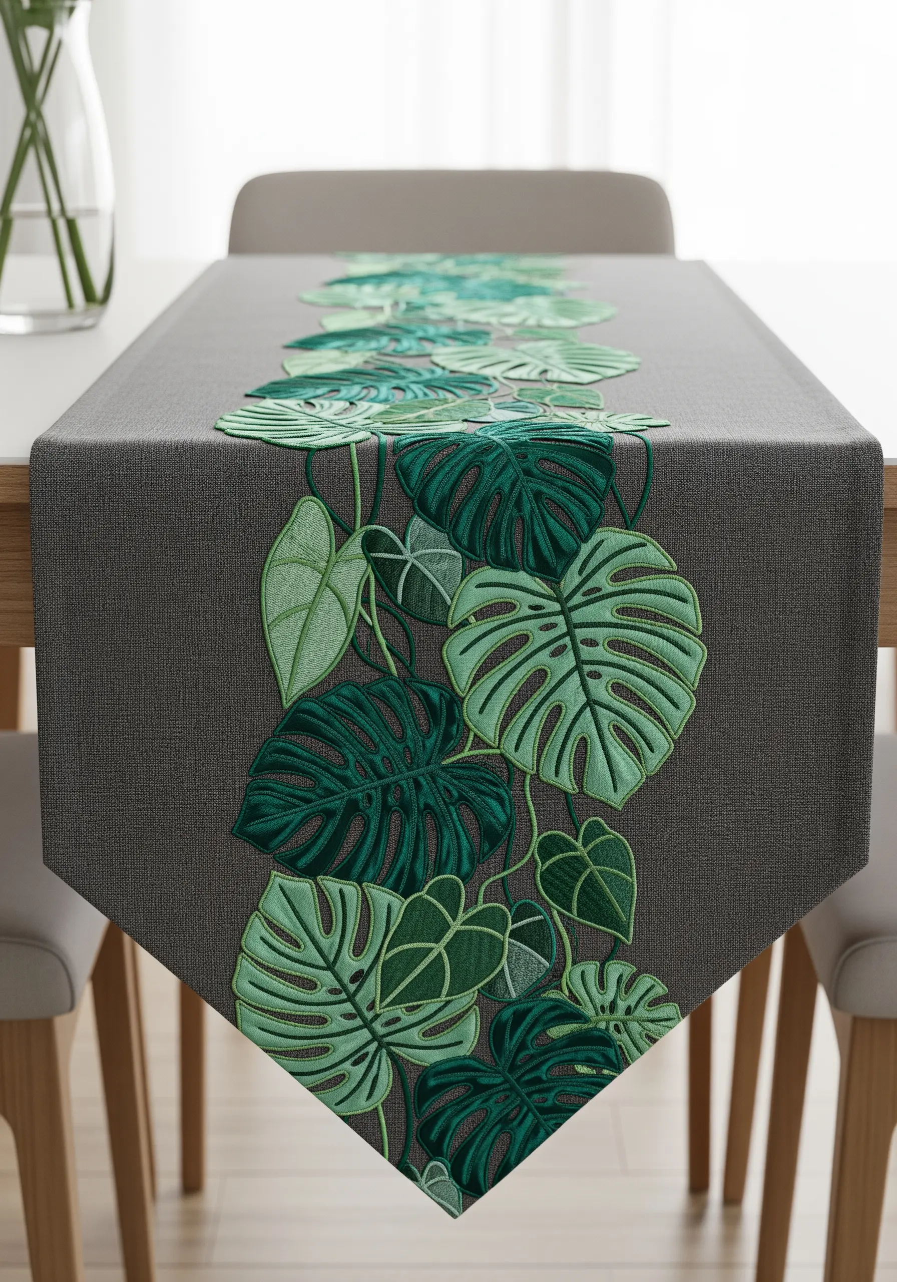A cascade of green monstera leaves embroidered down the center of a grey table runner.