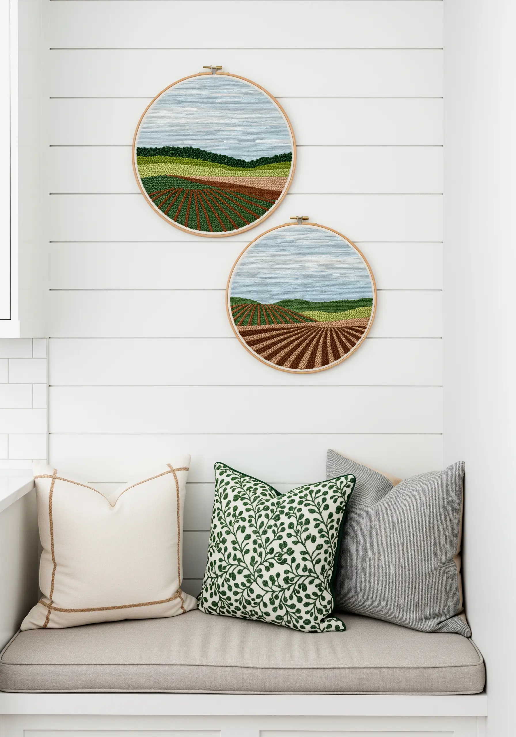 Two embroidery hoops depicting rolling fields and hills with painterly stitchwork.