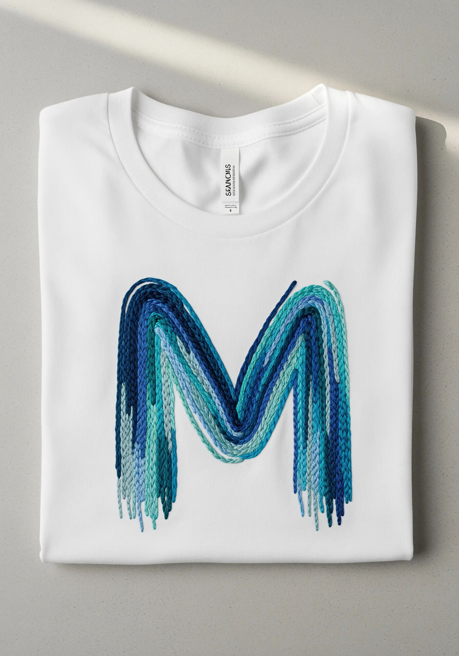 Letter 'M' embroidered with thick, chunky blue and teal yarn, creating a bold, textural effect.