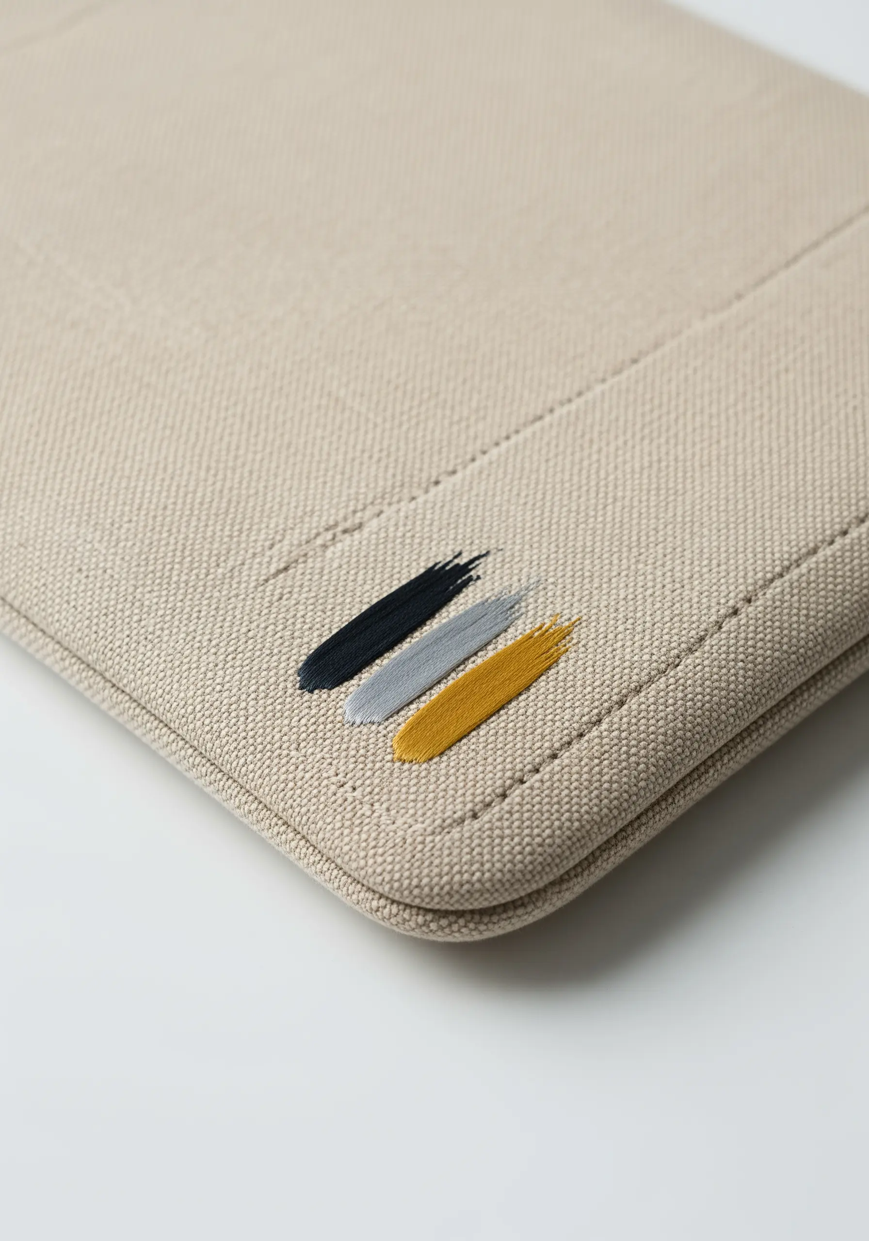 Three abstract, paint-like strokes embroidered in black, gray, and yellow on a canvas case.