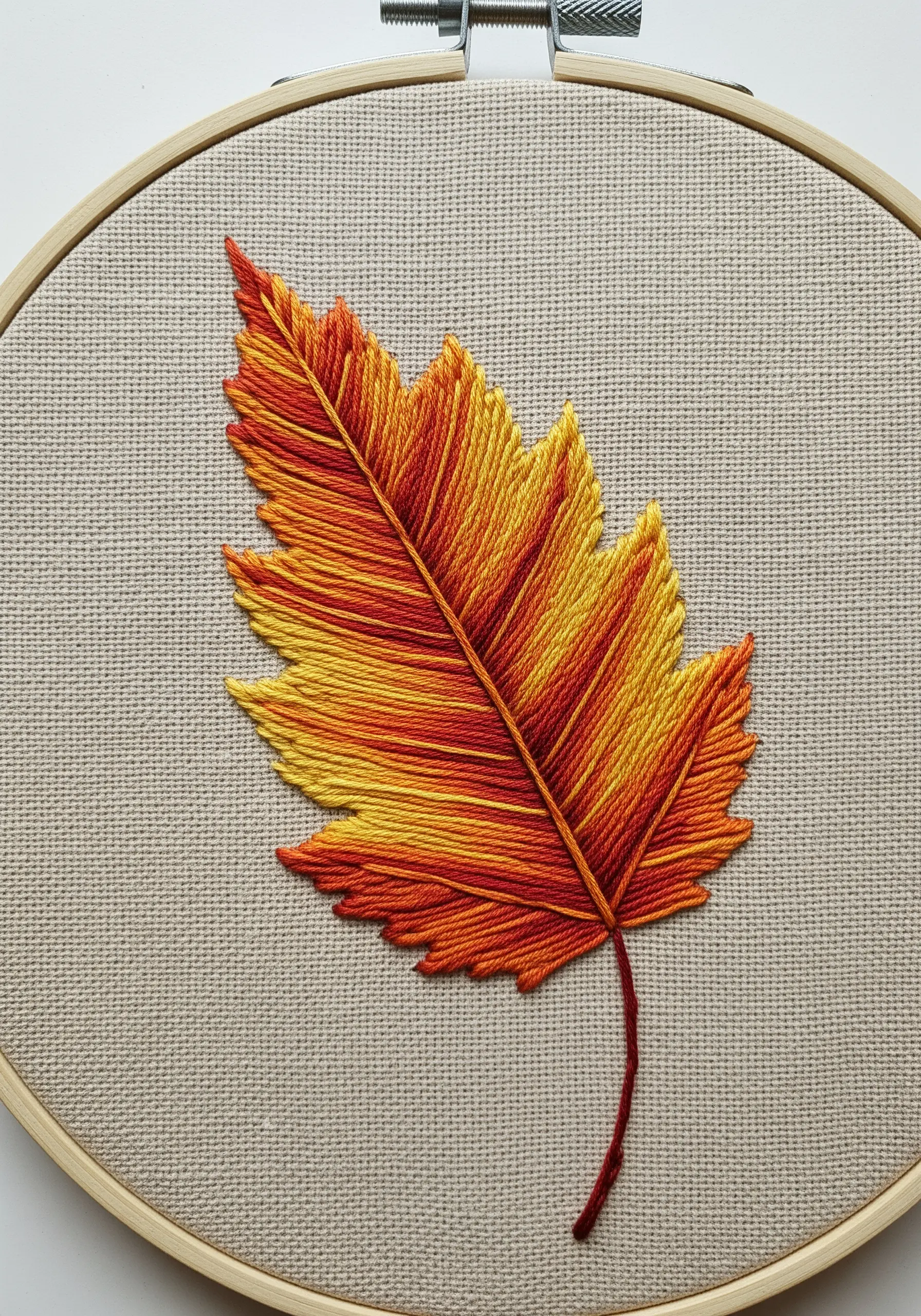 An autumn leaf embroidered with a smooth gradient of yellow, orange, and red thread.