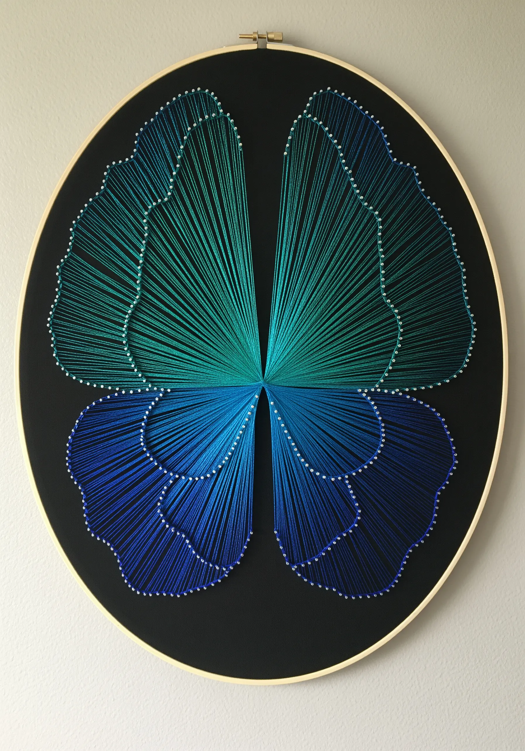 A string art butterfly with wings that blend from deep blue to bright teal on black fabric.