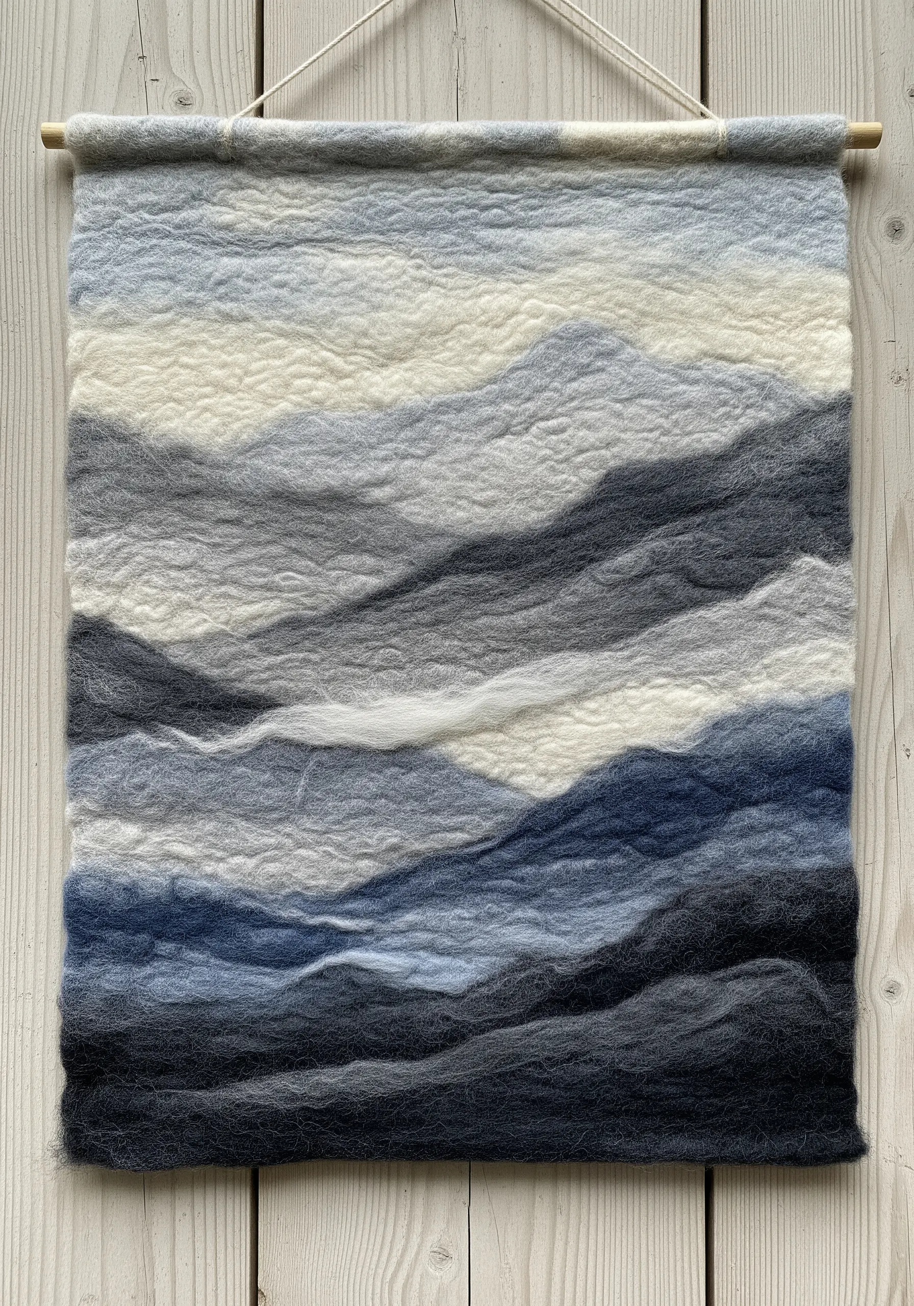 A needle-felted wool painting of layered blue and grey mountain ranges.