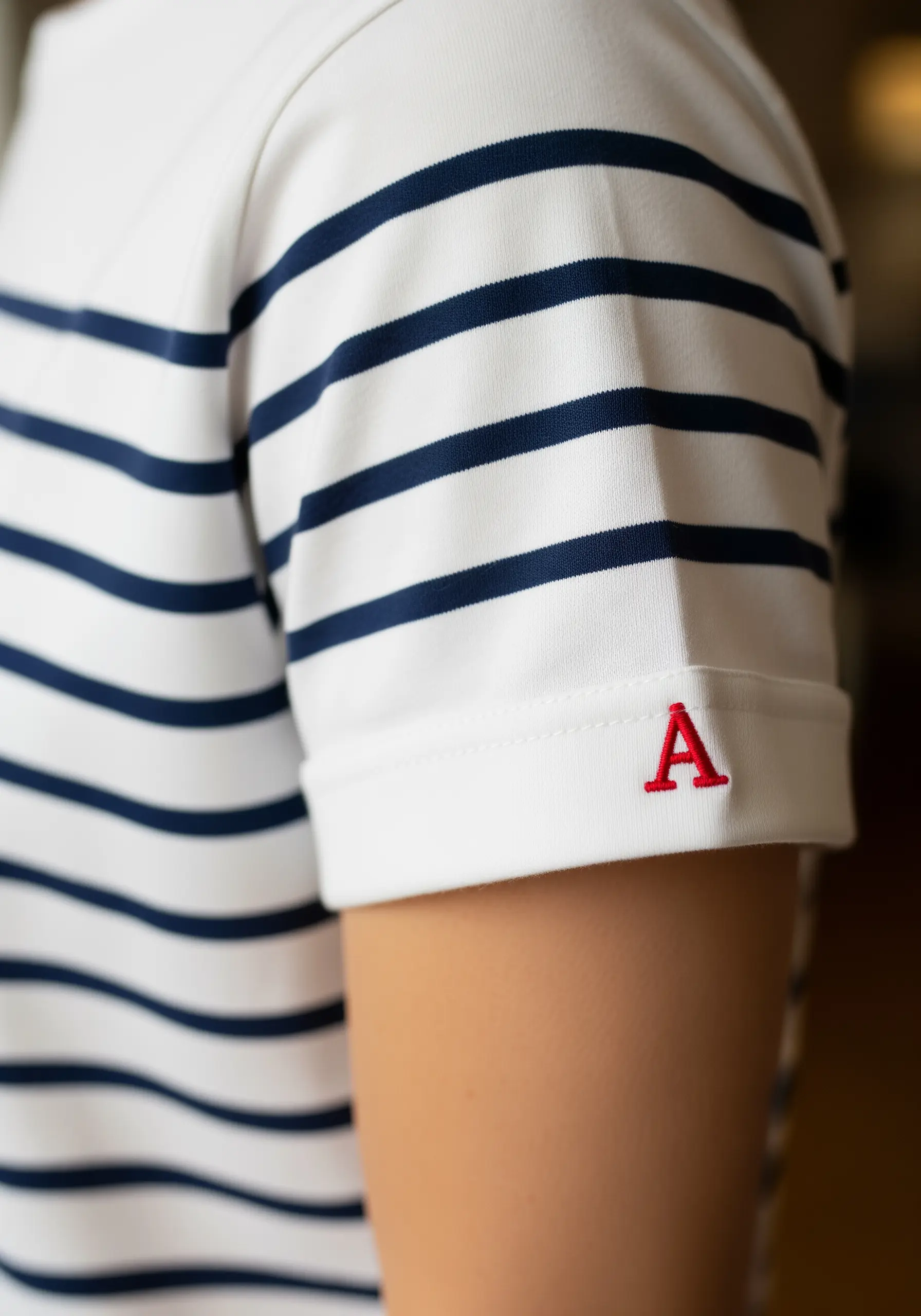 A small, classic red letter 'A' in a crisp satin stitch on the sleeve of a striped shirt.