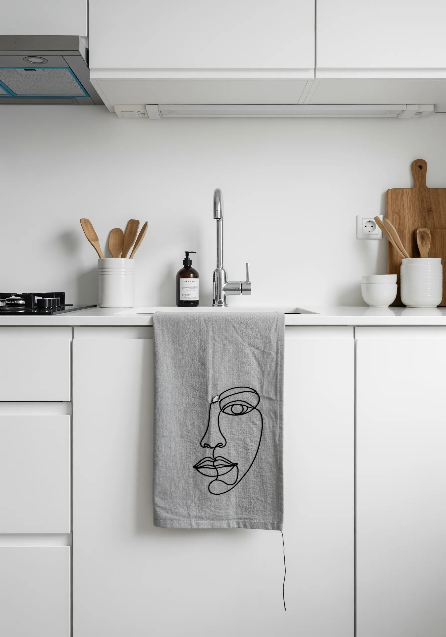 A minimalist abstract face embroidered in a single continuous black line on a grey towel.