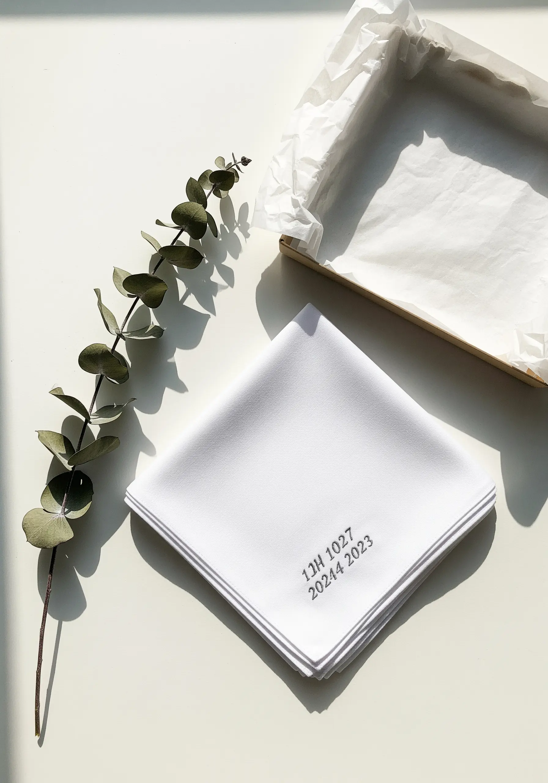 A special date and initials embroidered in tiny gray lettering on a white handkerchief.