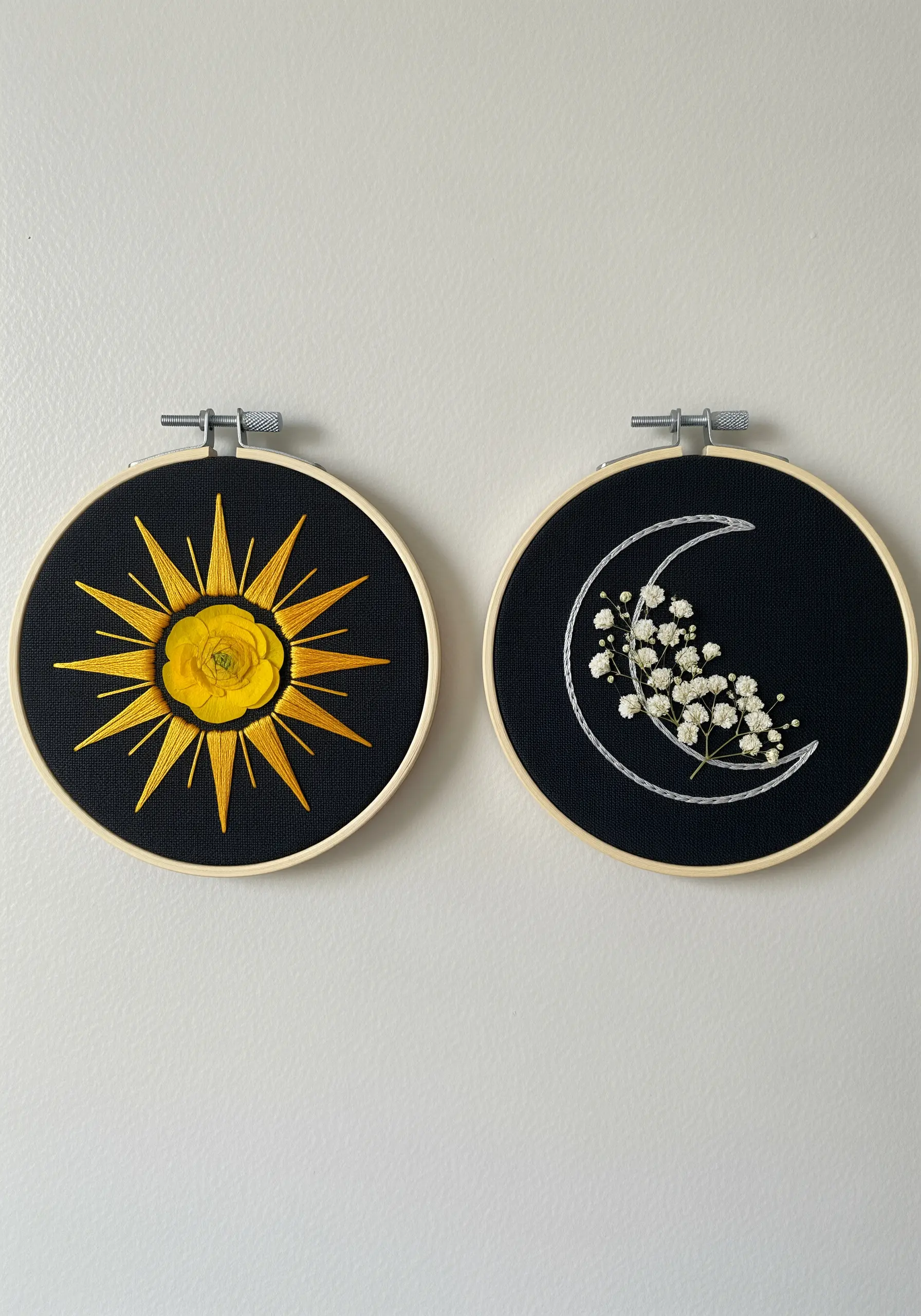 Two hoops on black fabric: a sun with a yellow flower and a moon with baby's breath.