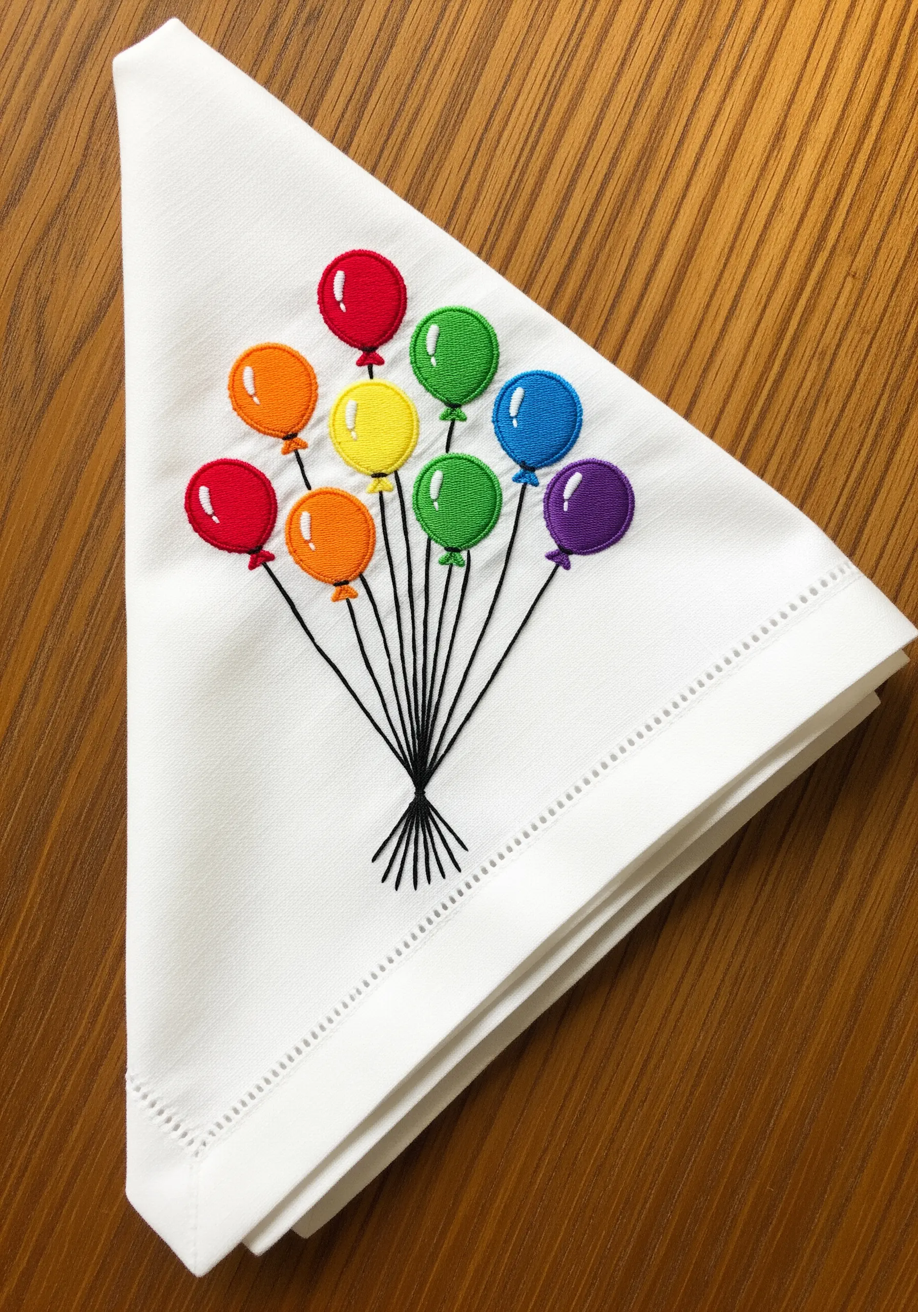 Smooth satin stitch balloons in rainbow colors with fine black strings on a white napkin.