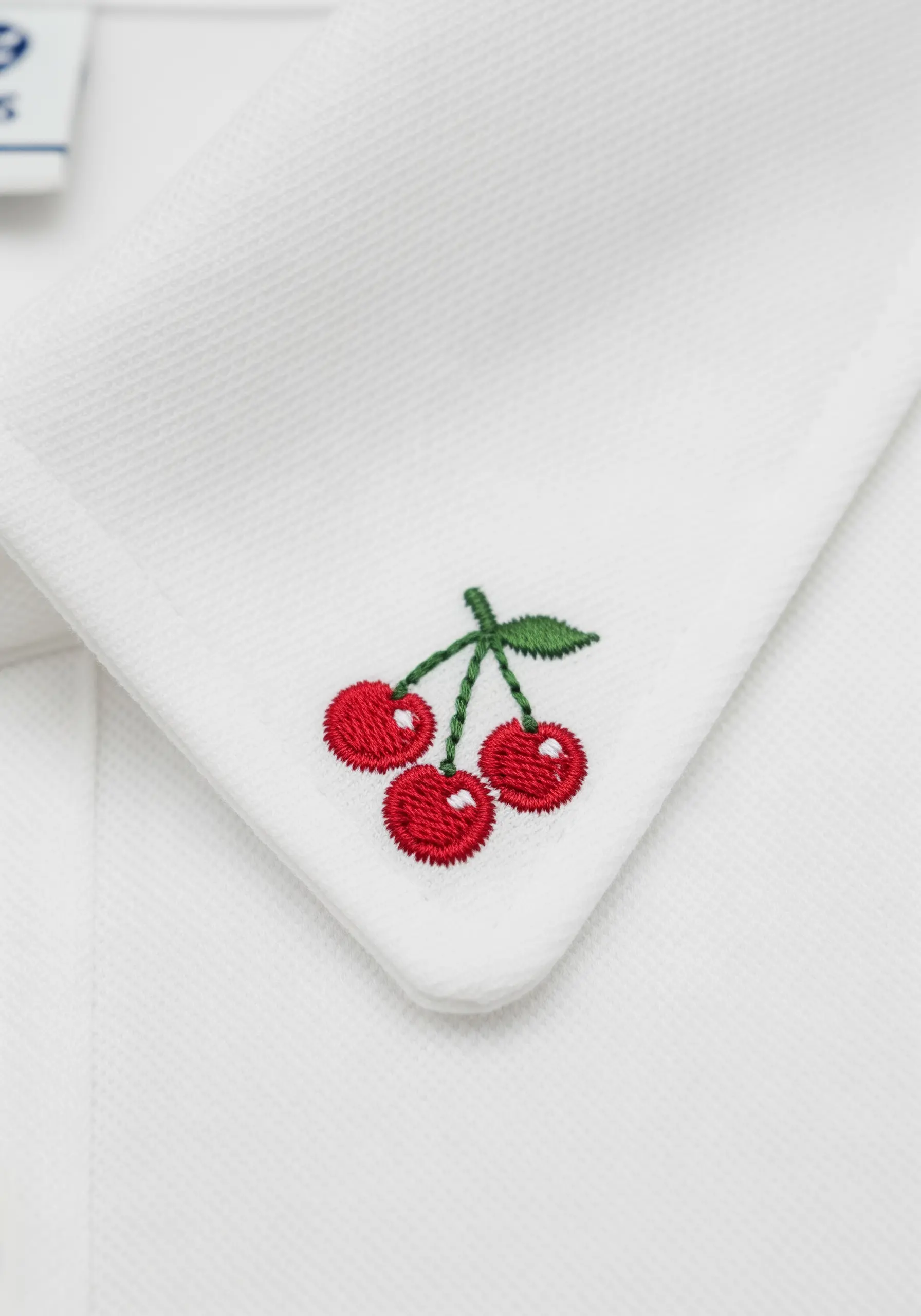 Three tiny embroidered red cherries on a white shirt collar.