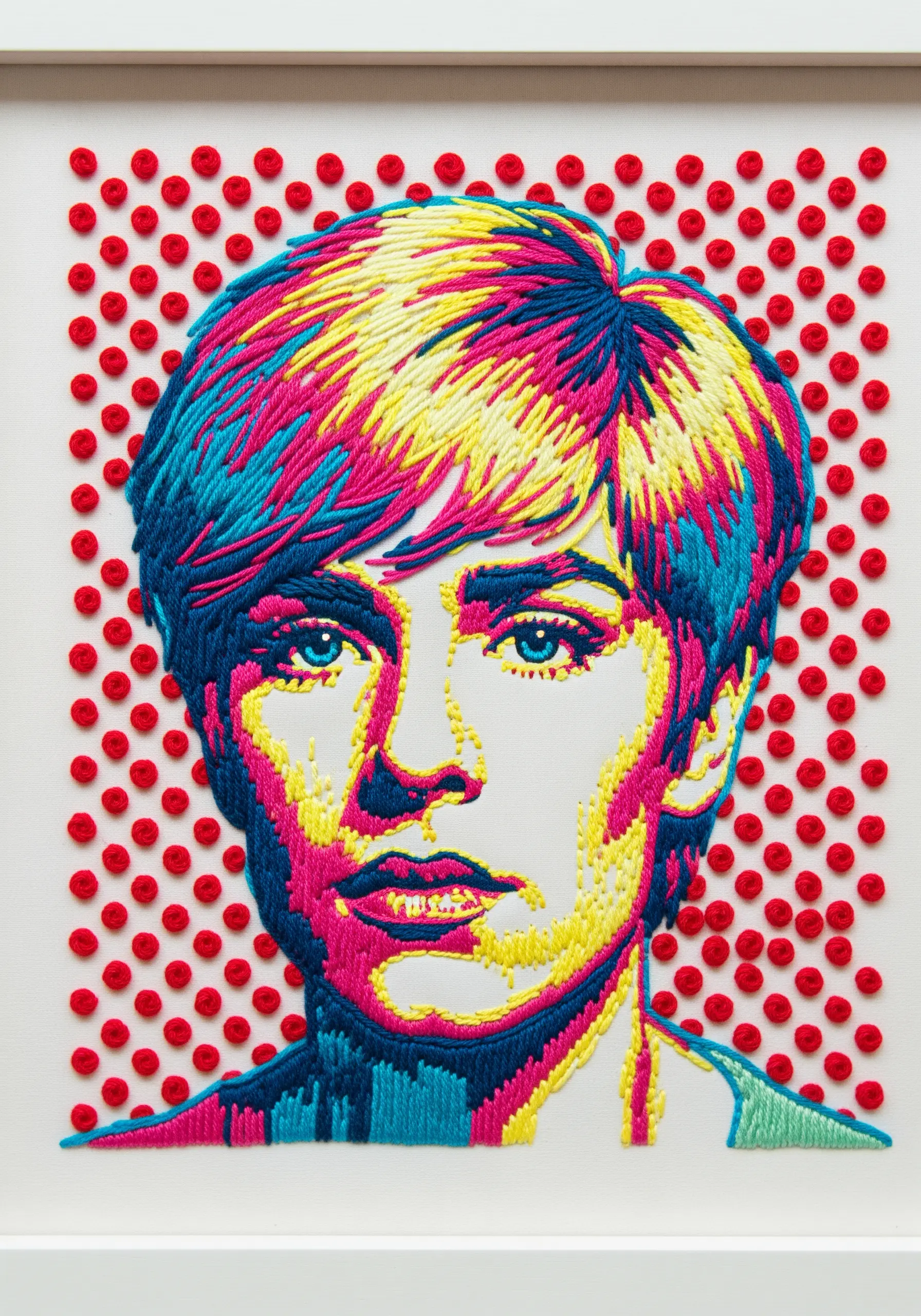 A pop art style embroidered portrait with bold blocks of yellow, pink, and blue thread.