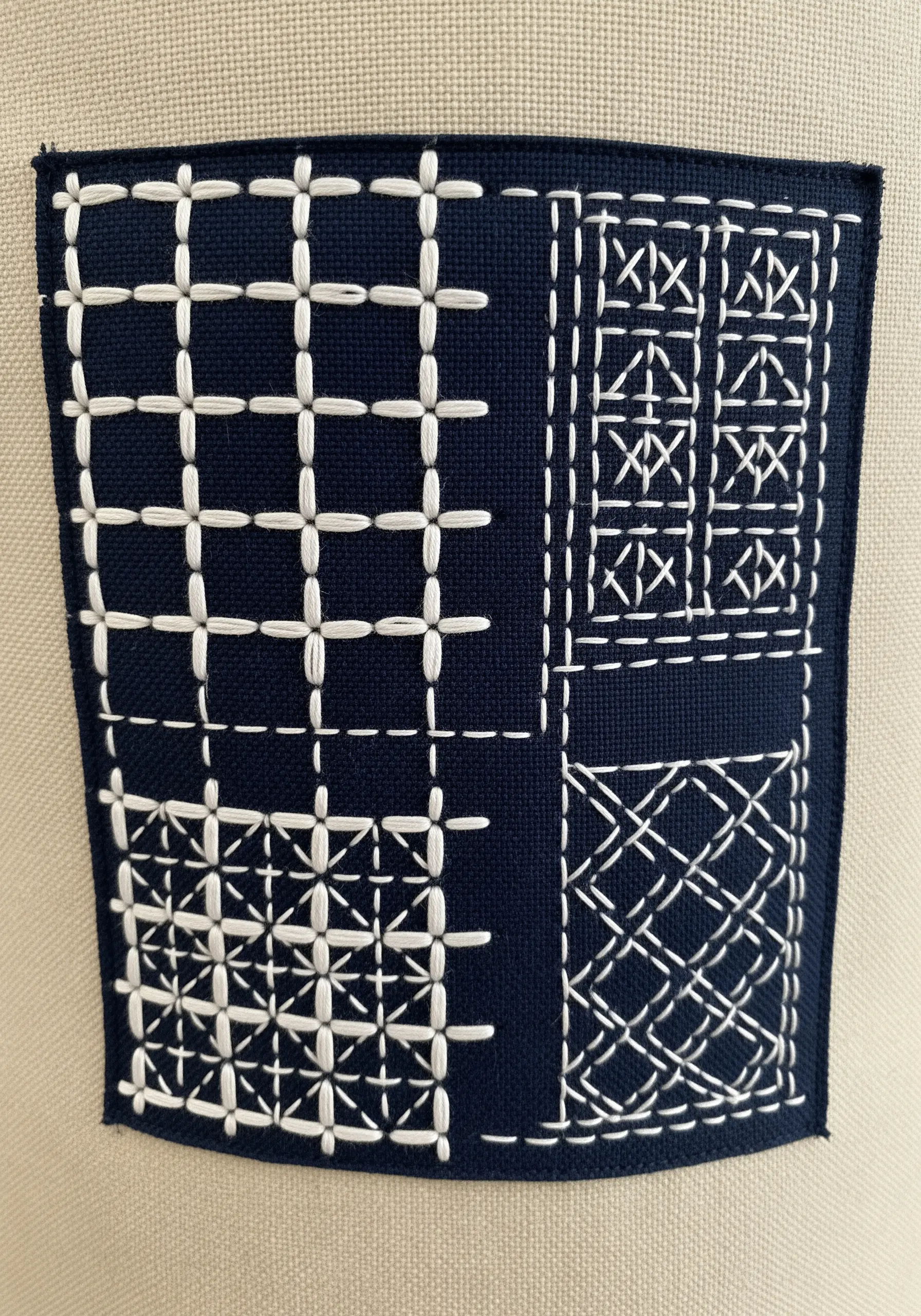 A dark blue fabric patch with geometric patterns stitched in white Sashiko embroidery.