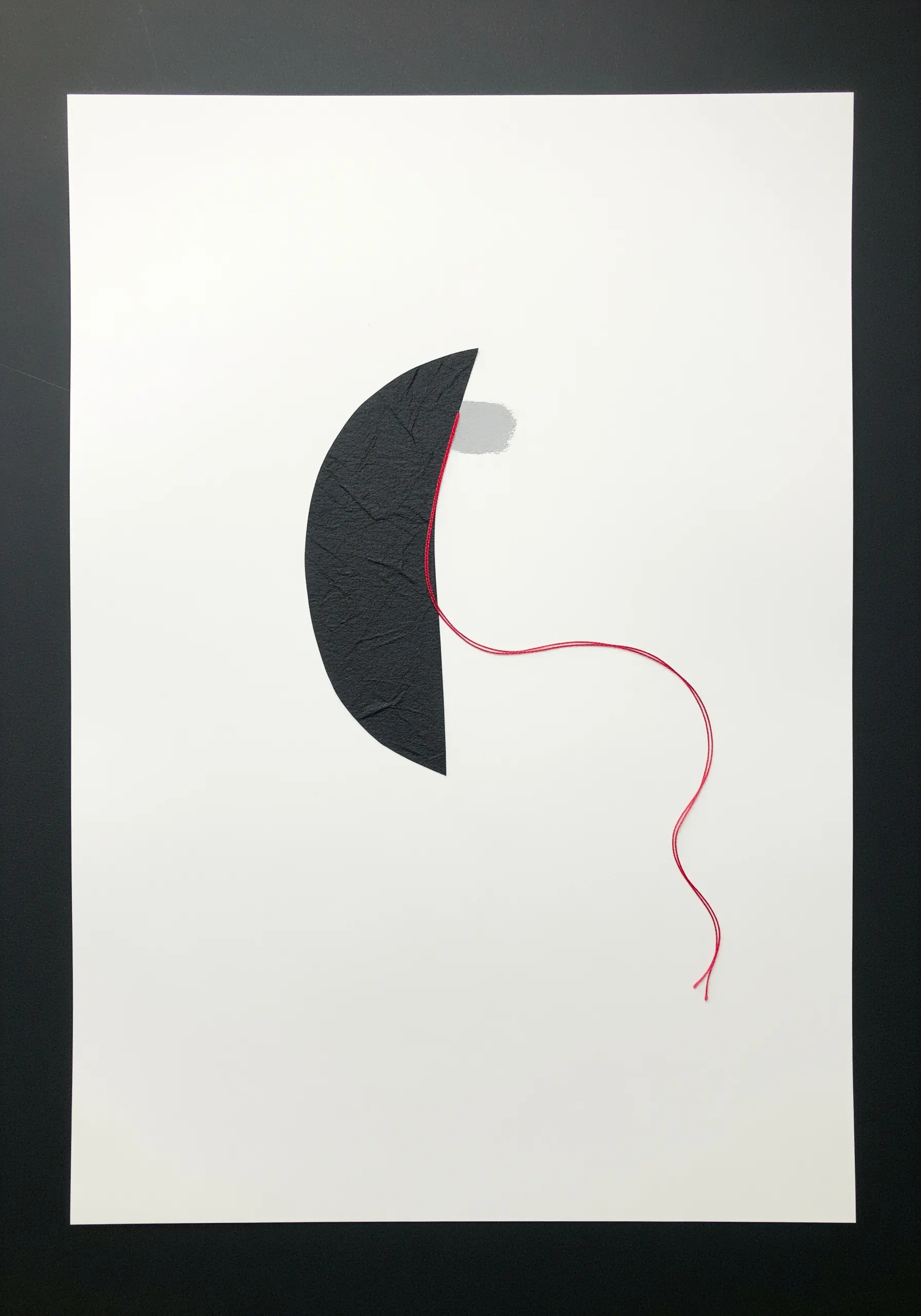 A minimalist artwork with a curved black paper shape and a single red thread on white paper.