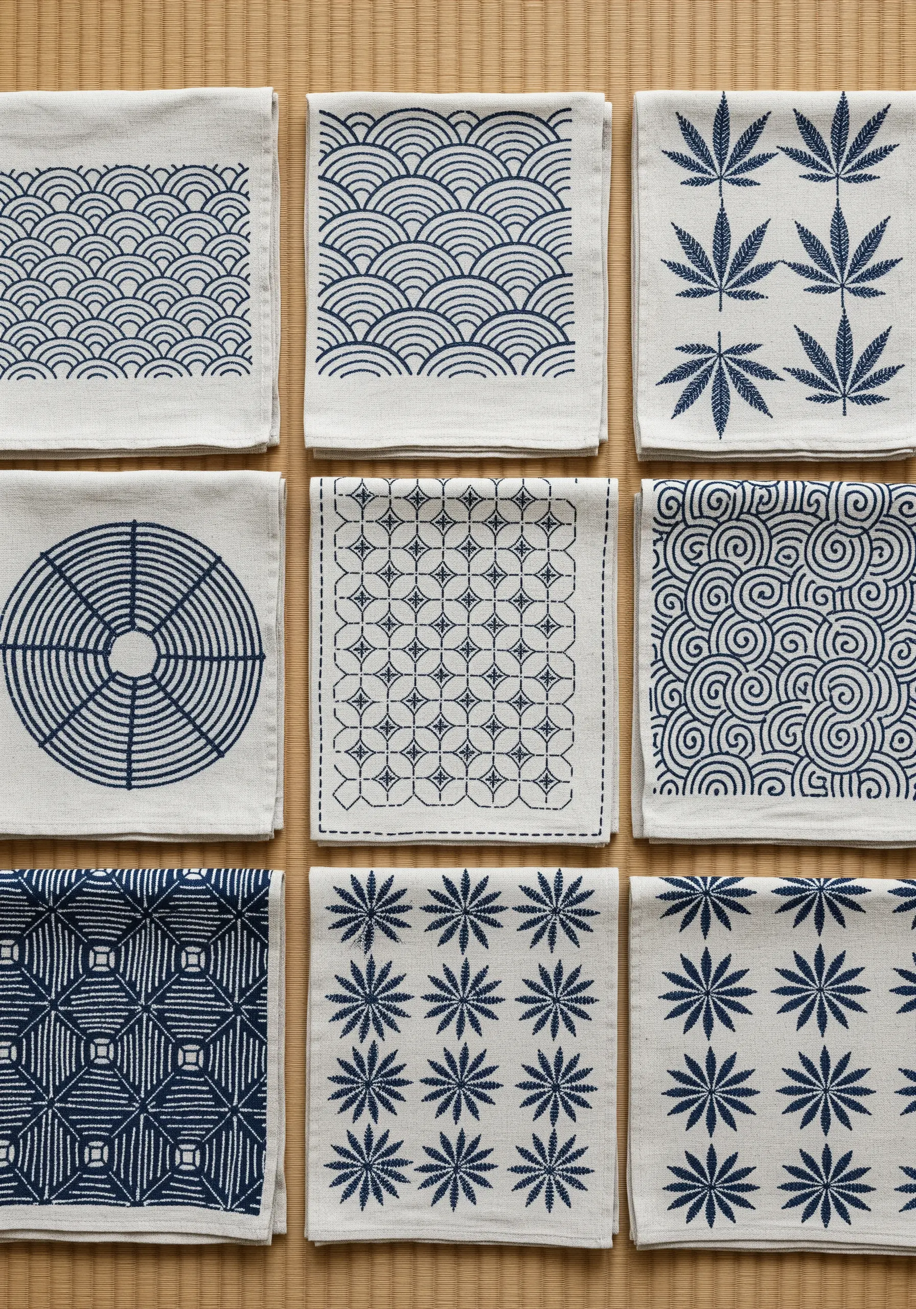 A collection of white linen squares with different geometric Sashiko patterns in blue thread.