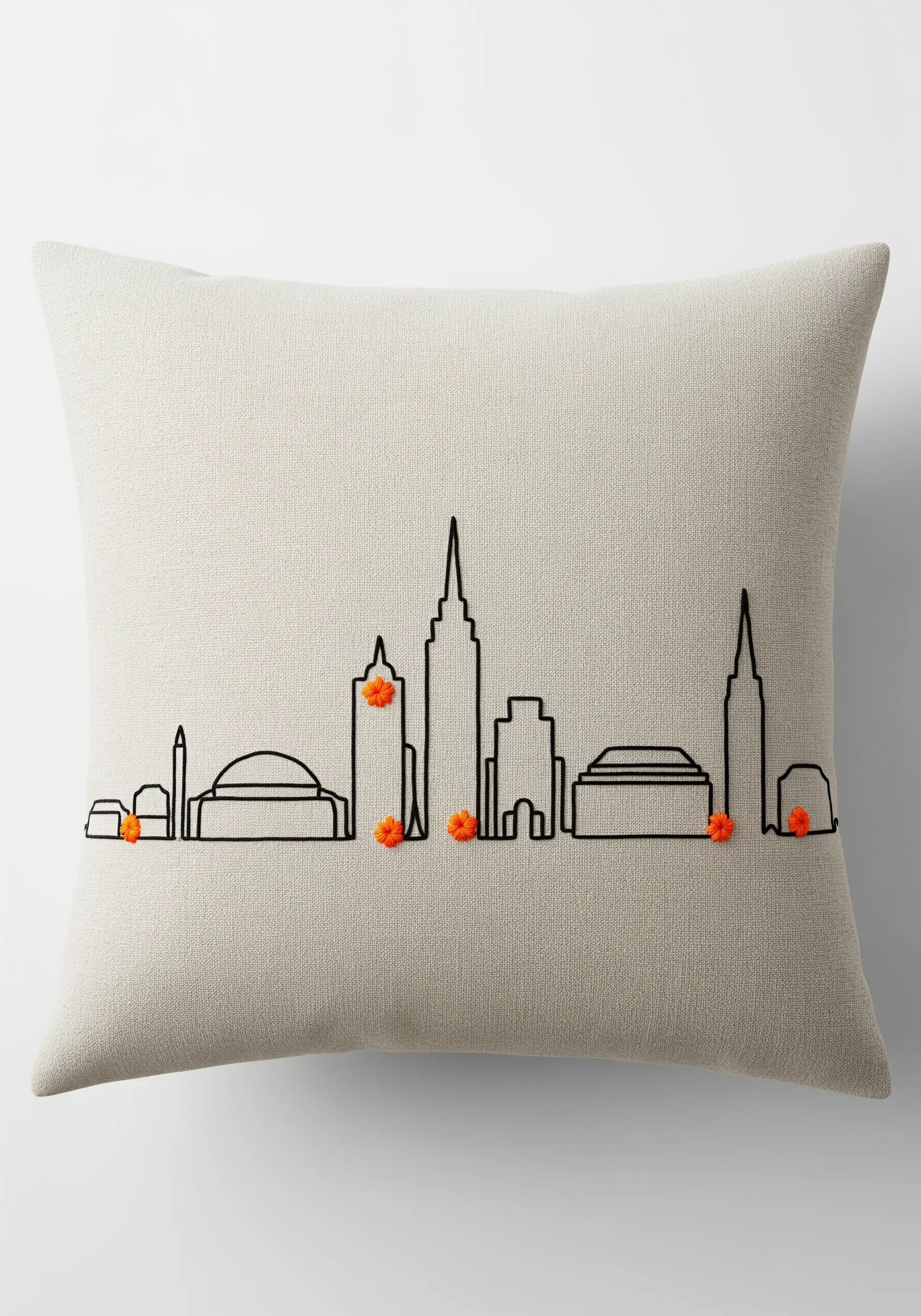 Minimalist black outline of a cityscape on a cream pillow with orange French knot accents.