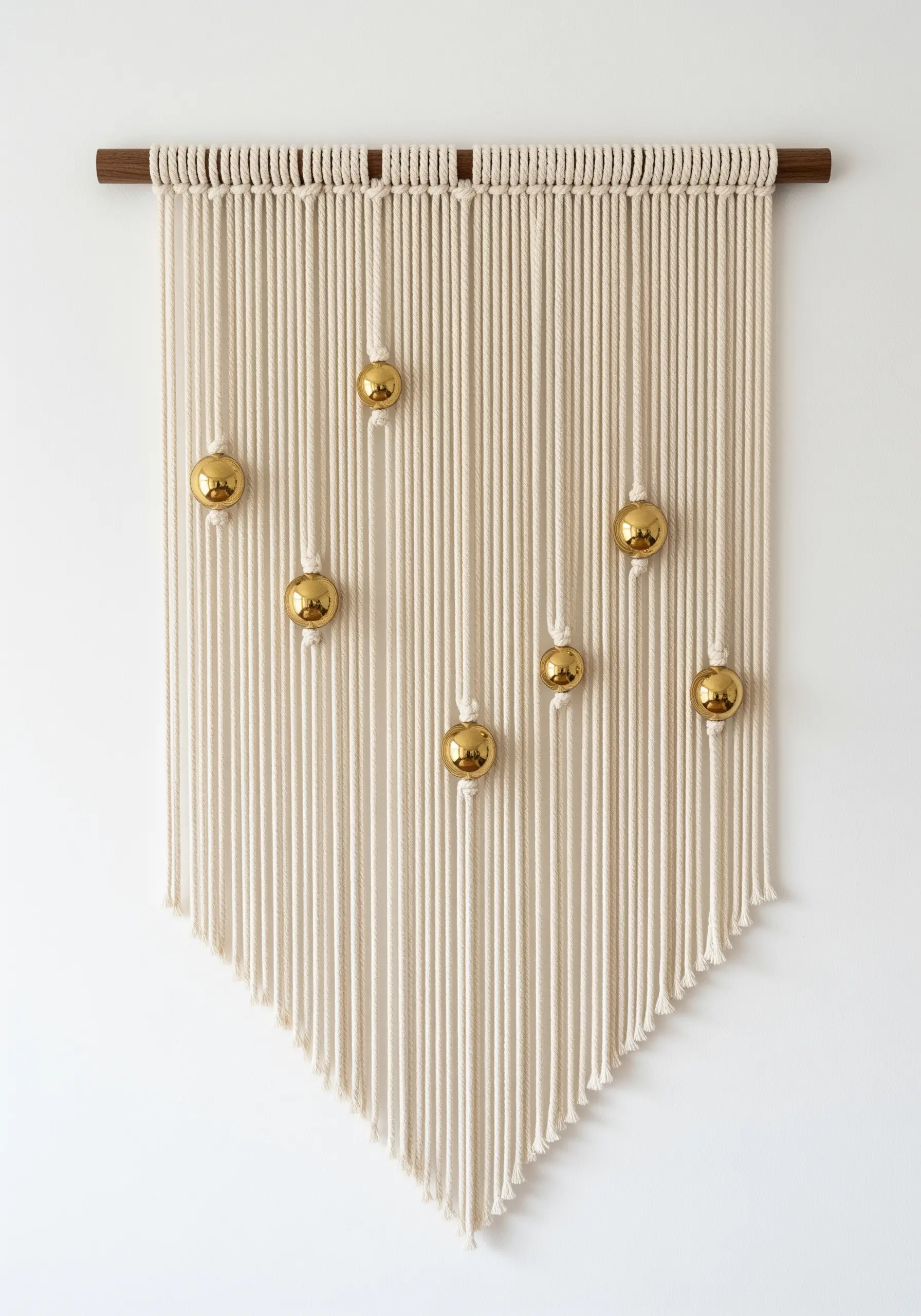 A minimalist macrame wall hanging with gold beads placed at varying heights.
