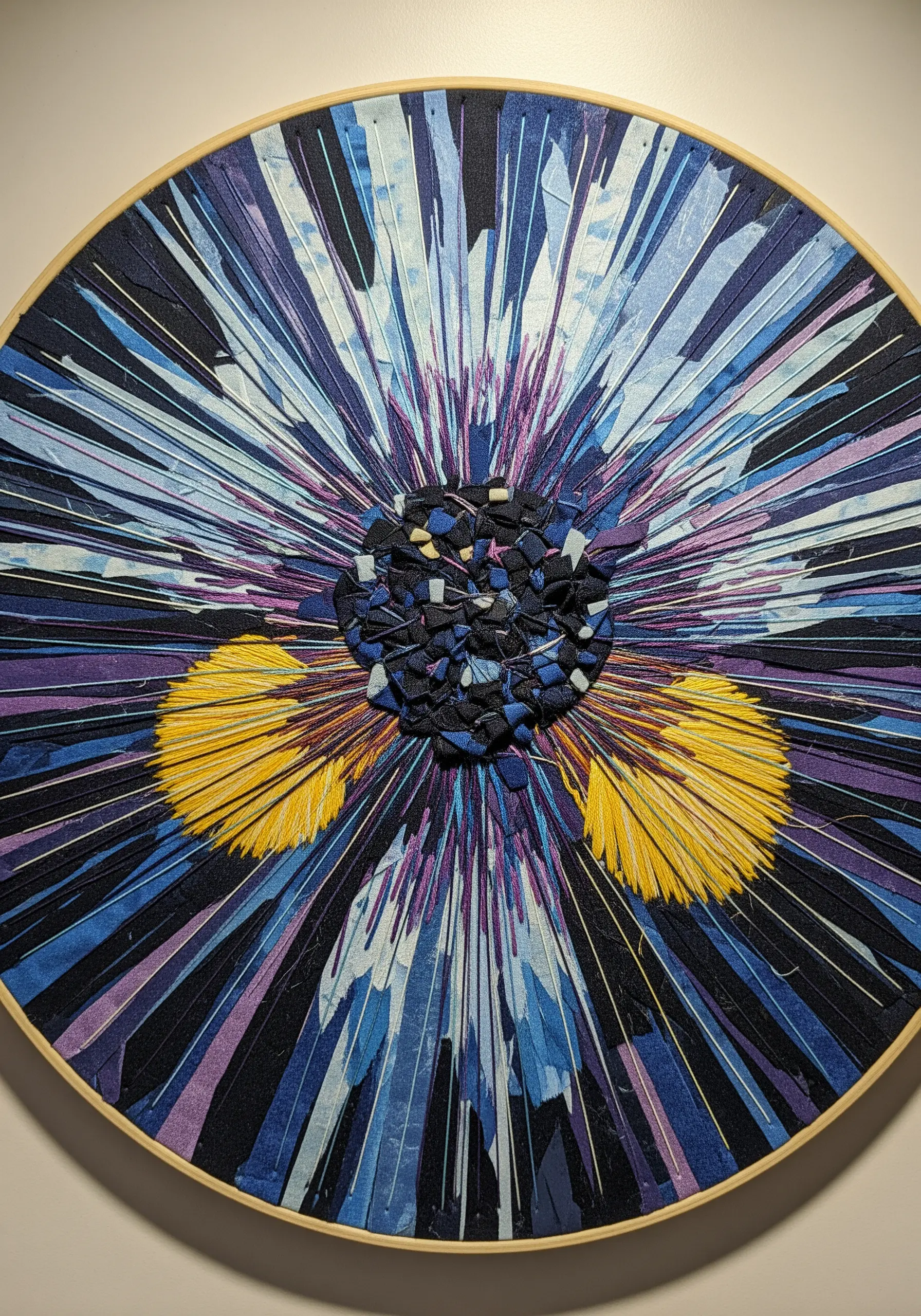 A dynamic hoop art piece with fabric shards arranged radially around a textured center.