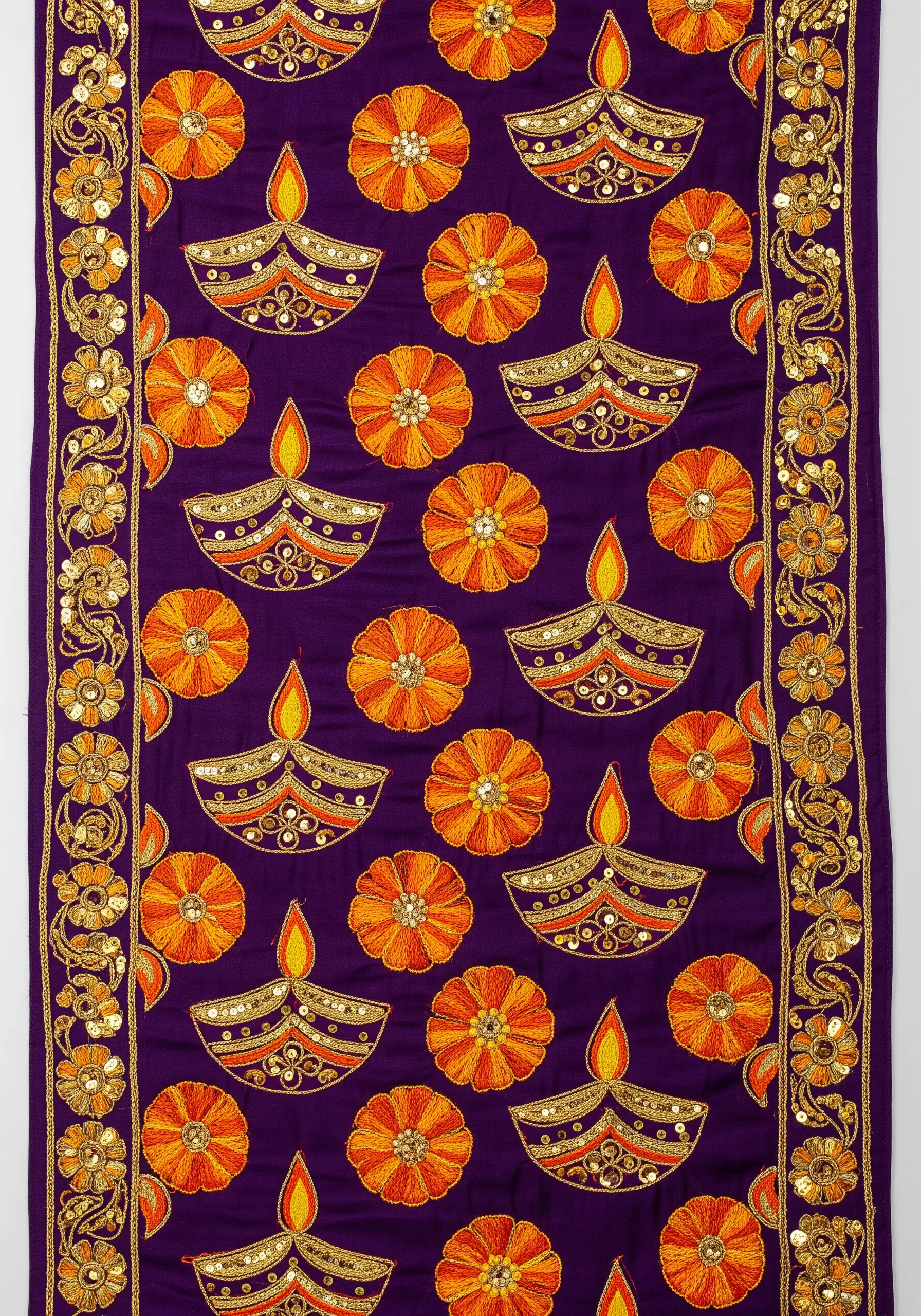 Embroidered Diwali diyas and marigolds with sequins on a purple table runner.