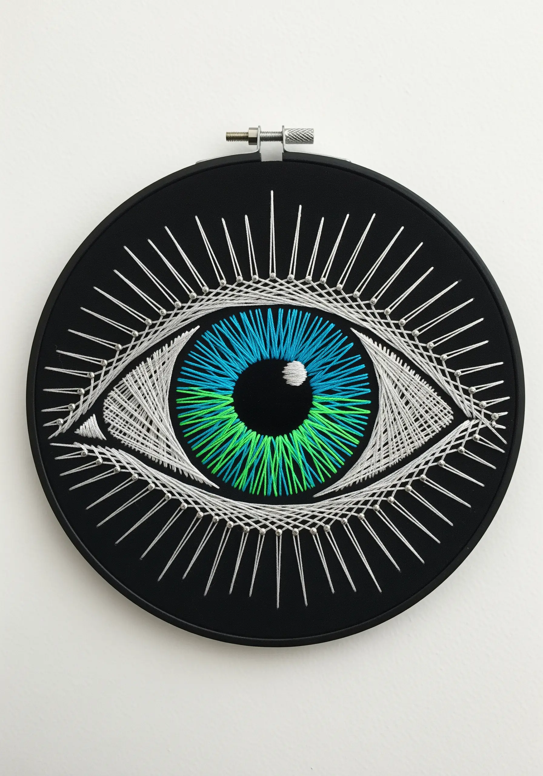 A stylized embroidered eye with a blue and green gradient iris and white lashes.