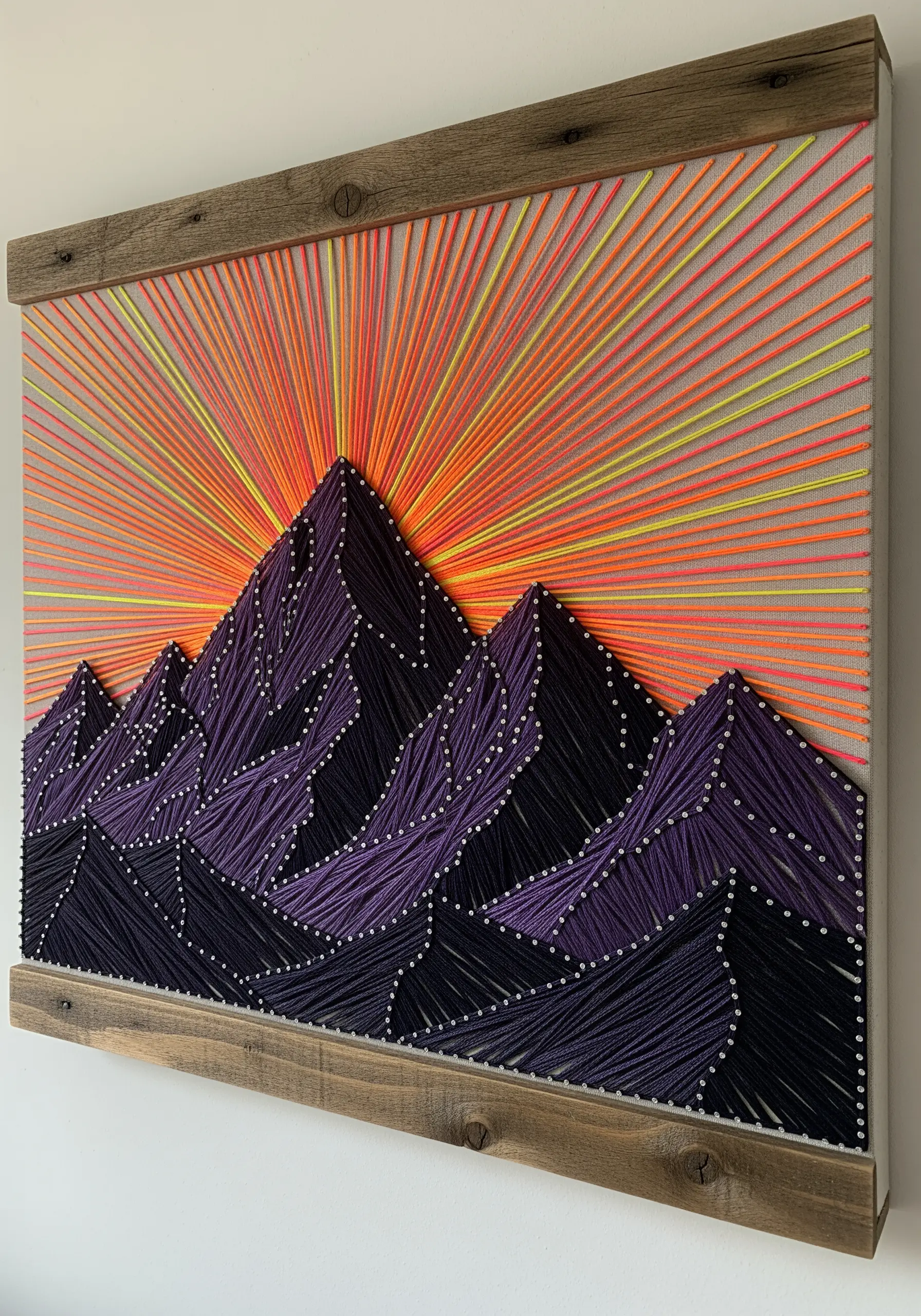 String art of a purple mountain range against a vibrant neon orange and yellow sunset.